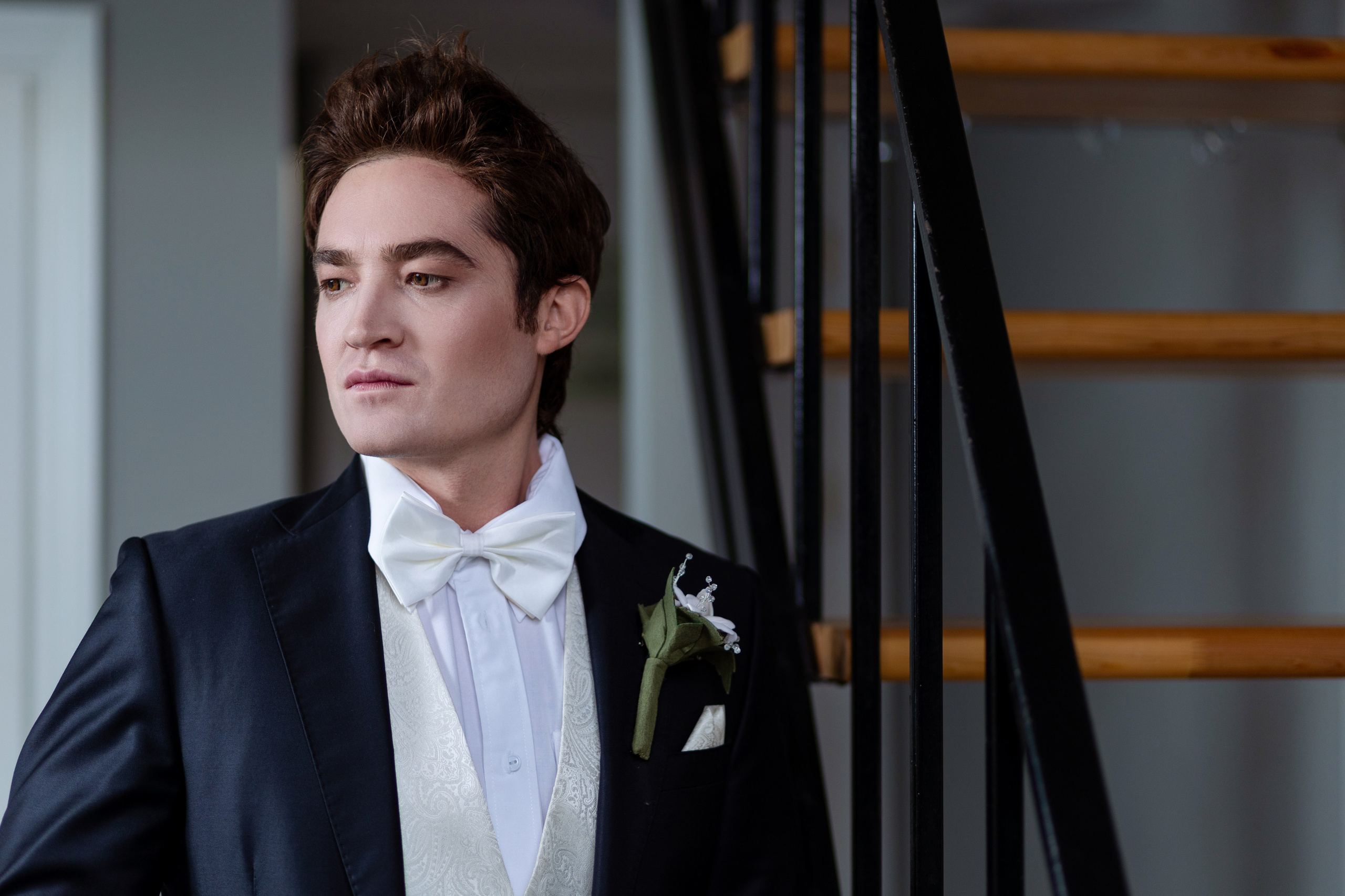 Жених стоит на фоне лестницы не во весь рост.