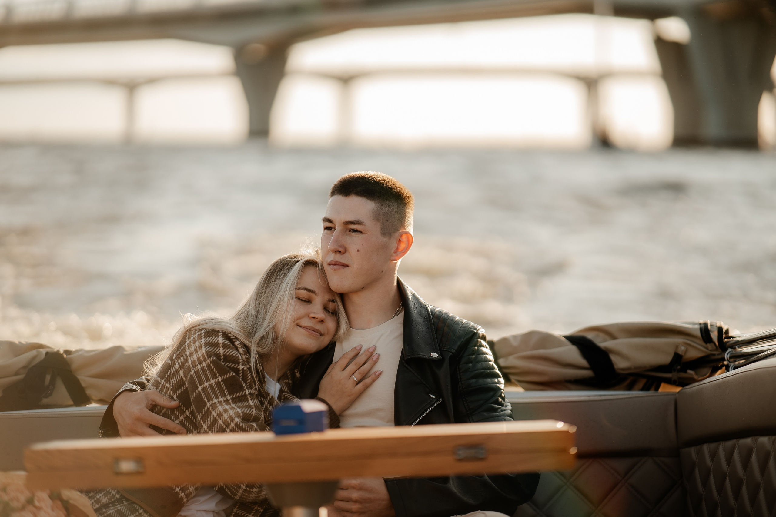 Молодая пара сидит на катере и обнимается в лучах закатного солнца