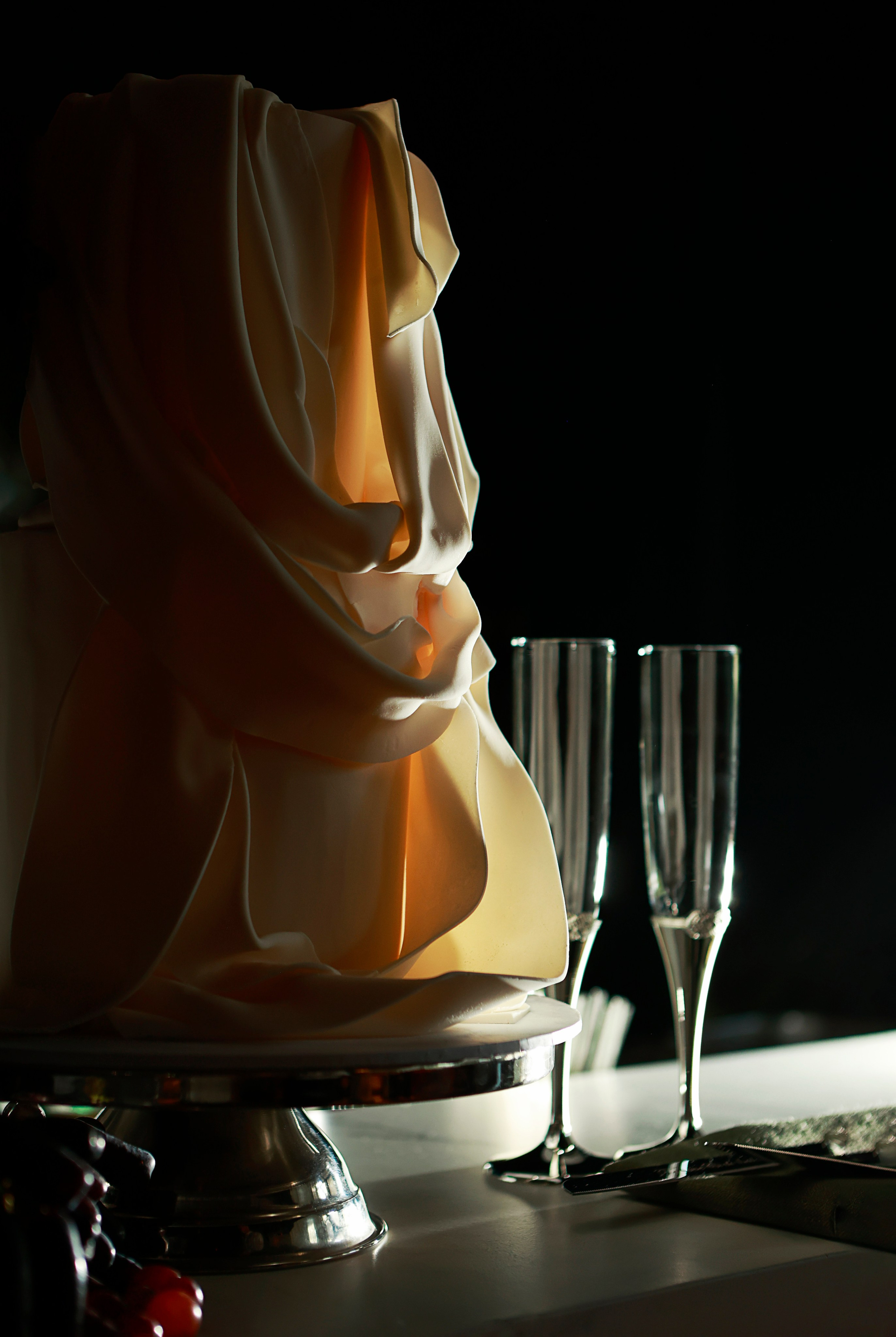 Sculptural luxury wedding cake with draped fondant and champagne glasses photographed in dramatic editorial light for premium event and brand imagery in Sydney