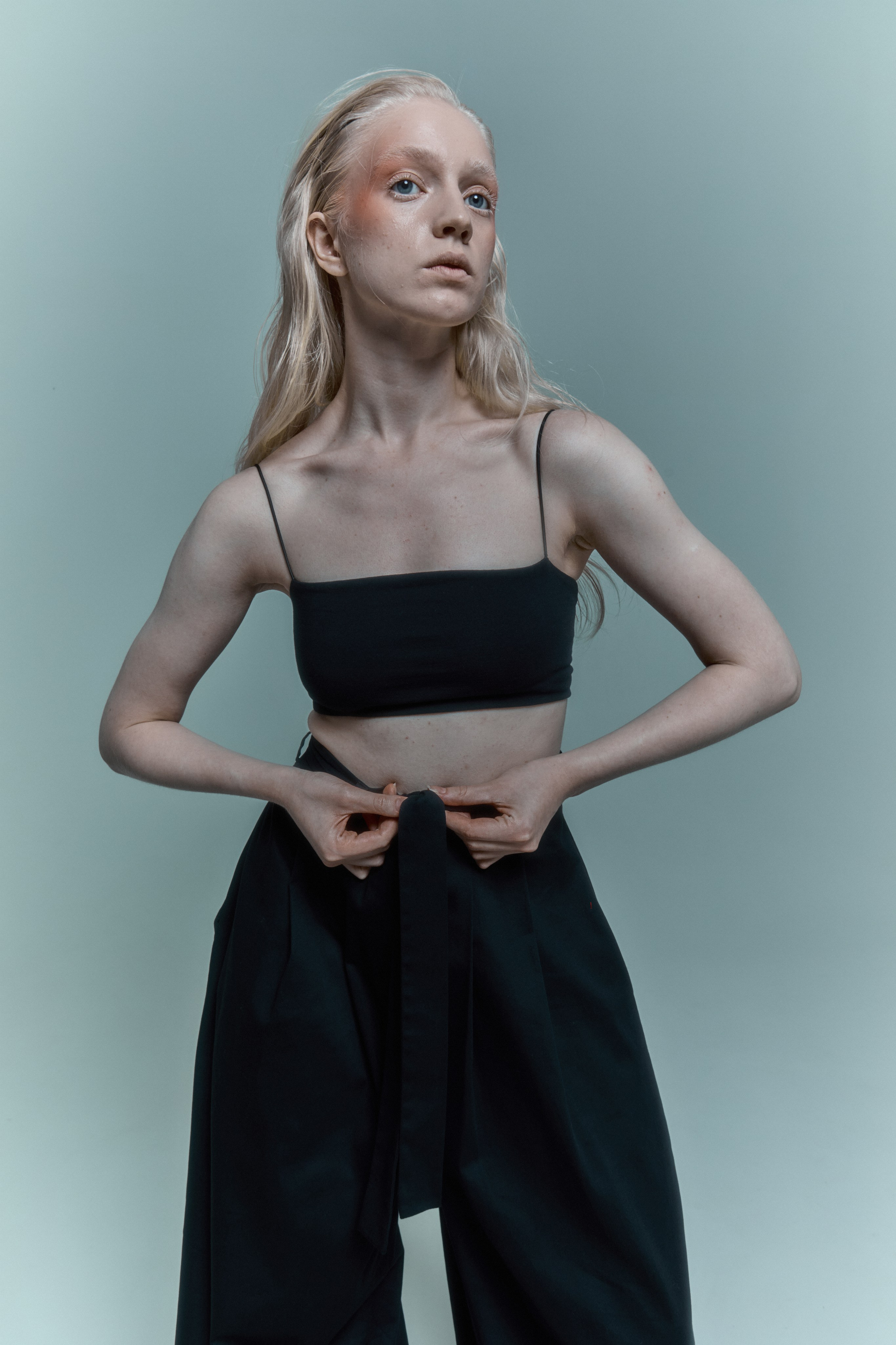 Девушка модель блондинка в черном топе и черных широких штанах