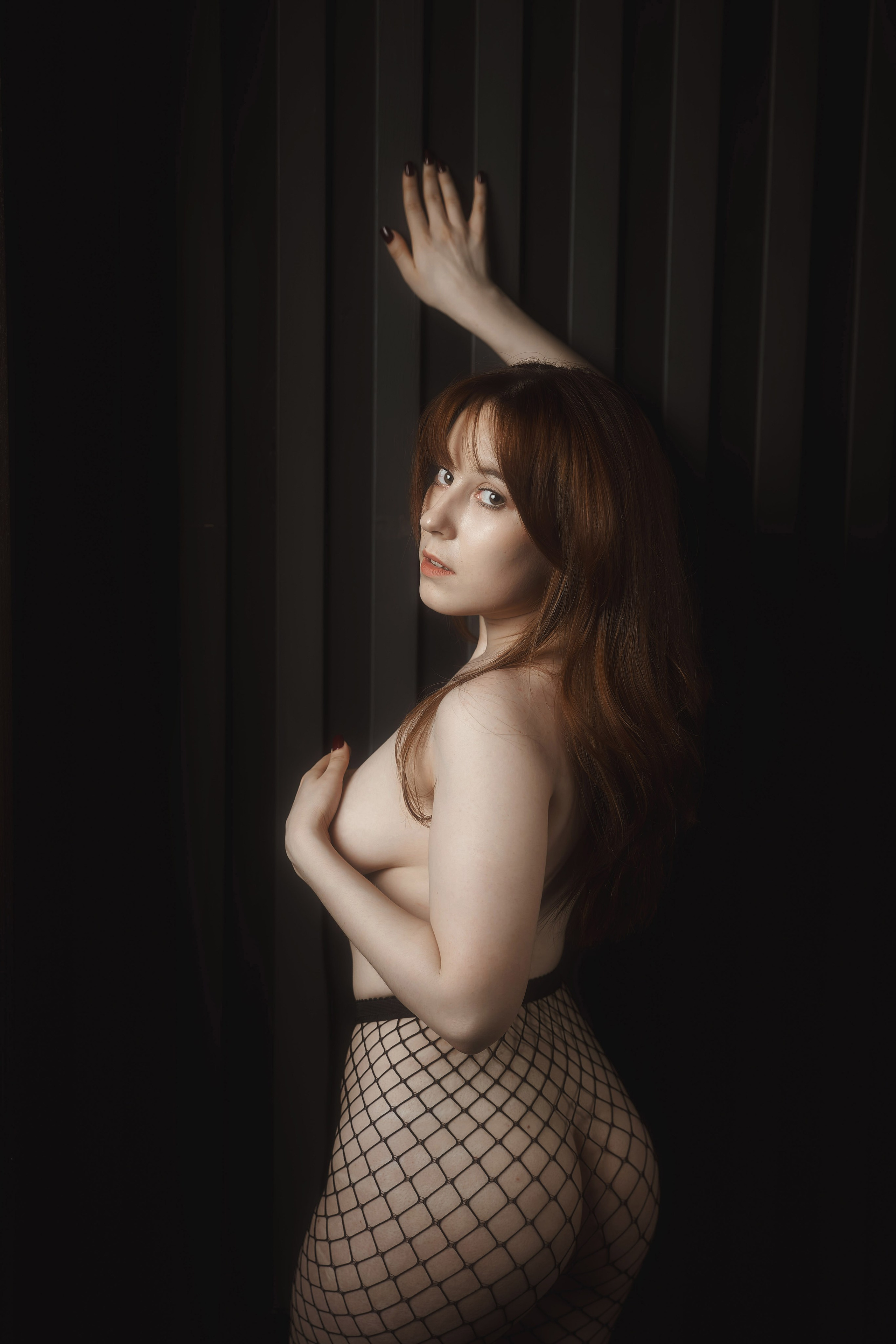 красивая молодая девушка в колготках в сеточку застенчиво прикрывает обнаженную грудь на фотосессии в стиле ню фотографа Евгения Опарина