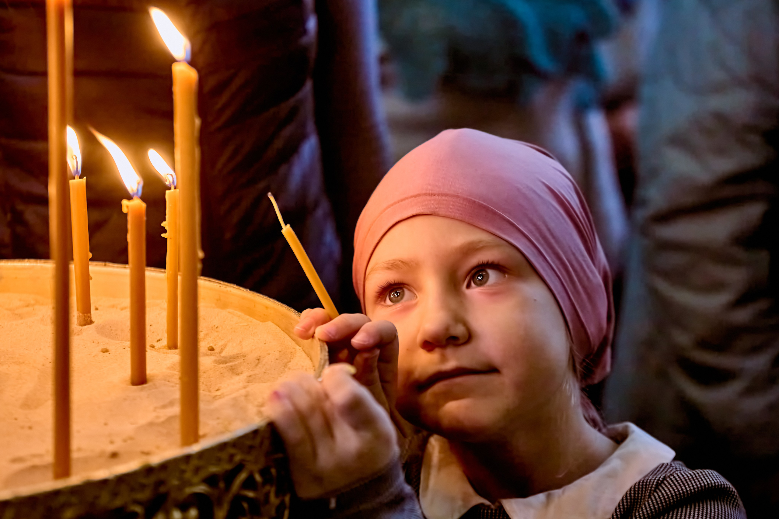 Маленькая девочка 6 лет стоит у подсвечника в размышлениях  о желании возжигать свечу