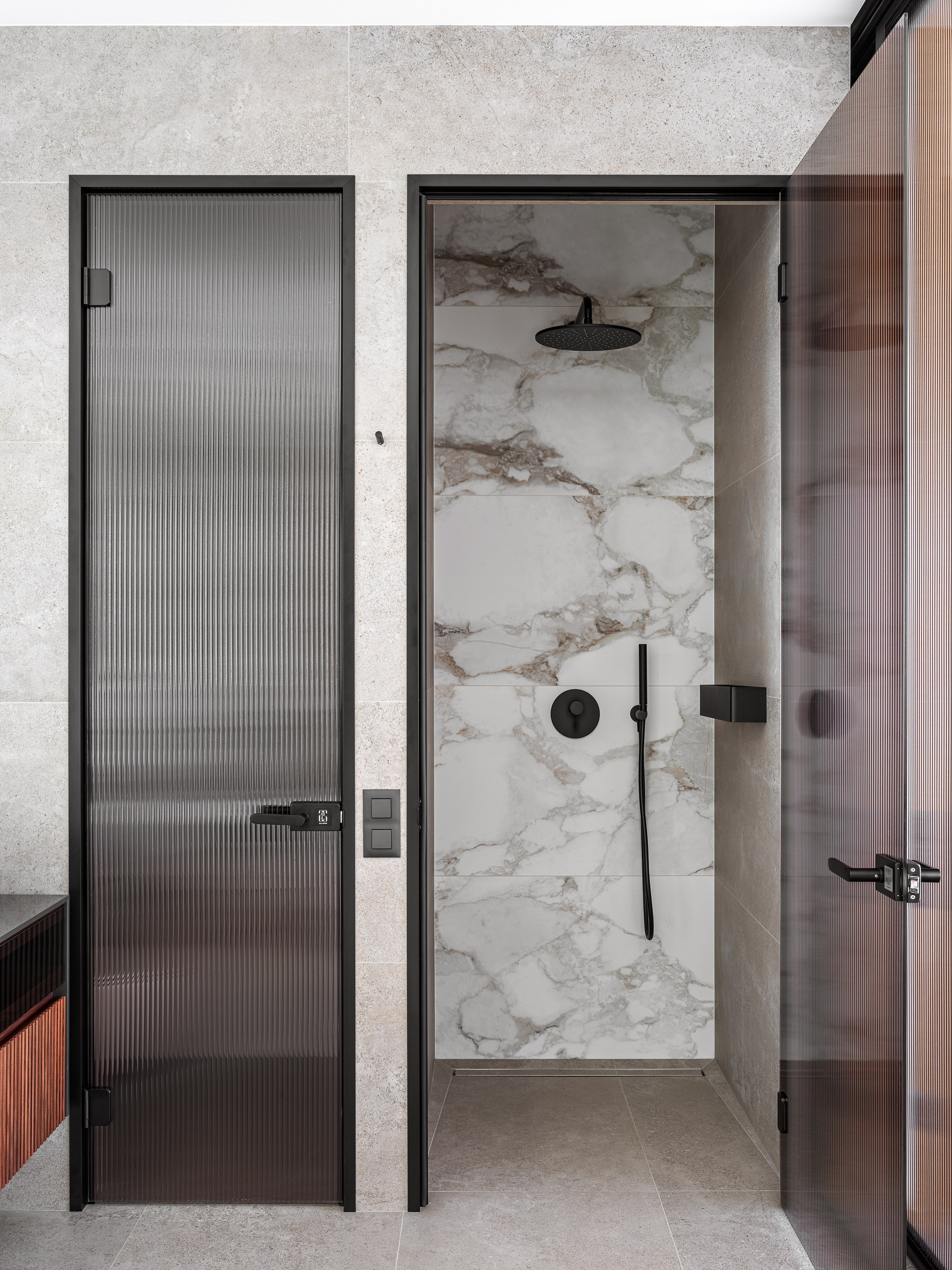 Ванная комната с душевой зоной, отделанной крупноформатной плиткой под мрамор, и матовыми стеклянными дверями в черных рамах. Элегантный современный дизайн разработан Ренатом Байчуковым и Алисей Кириенко, стилистика Екатерины Ракитиной, фото Сергея Денисенко.