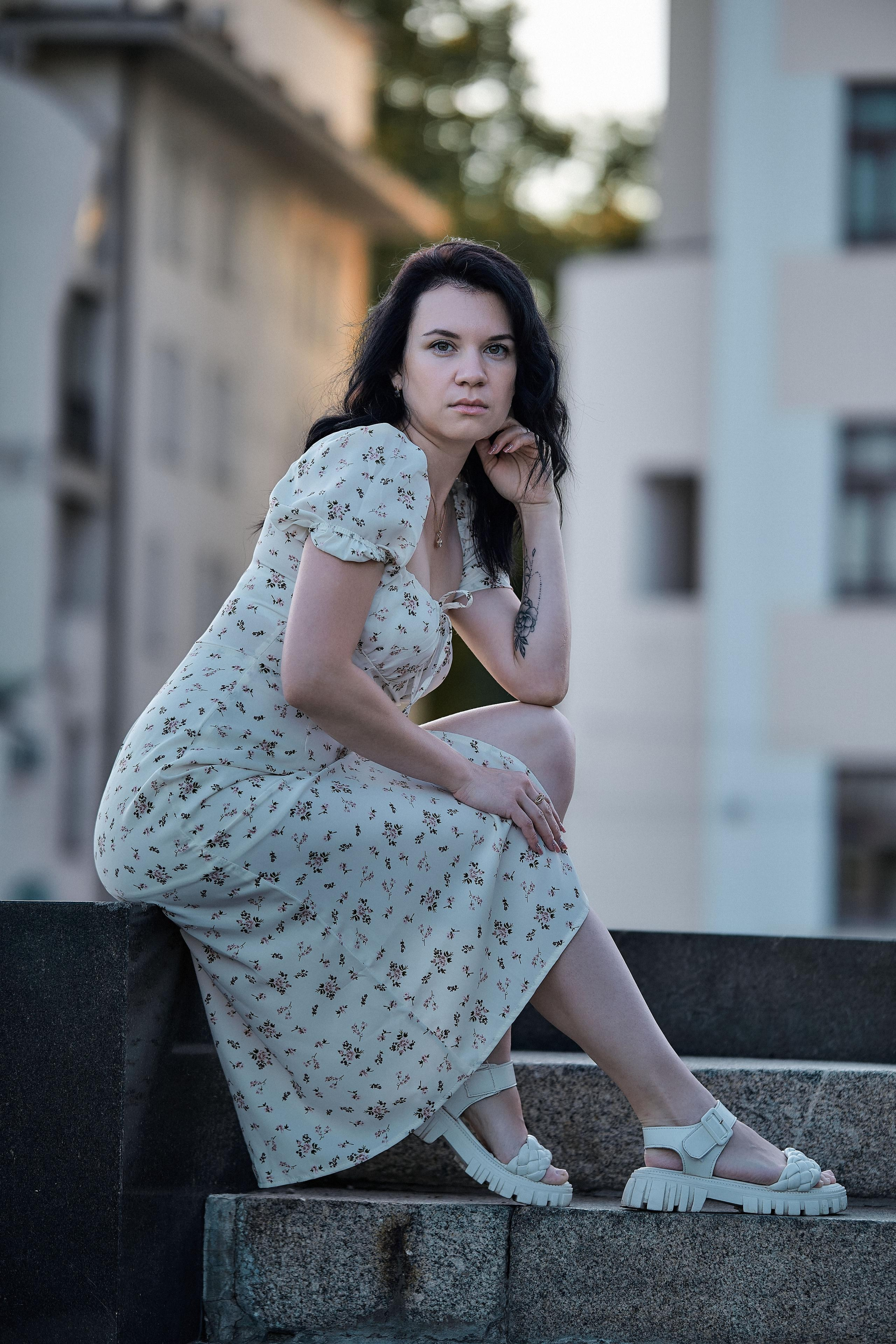 Романтичный образ в цветочном платье, сидящая поза на архитектурном фоне.