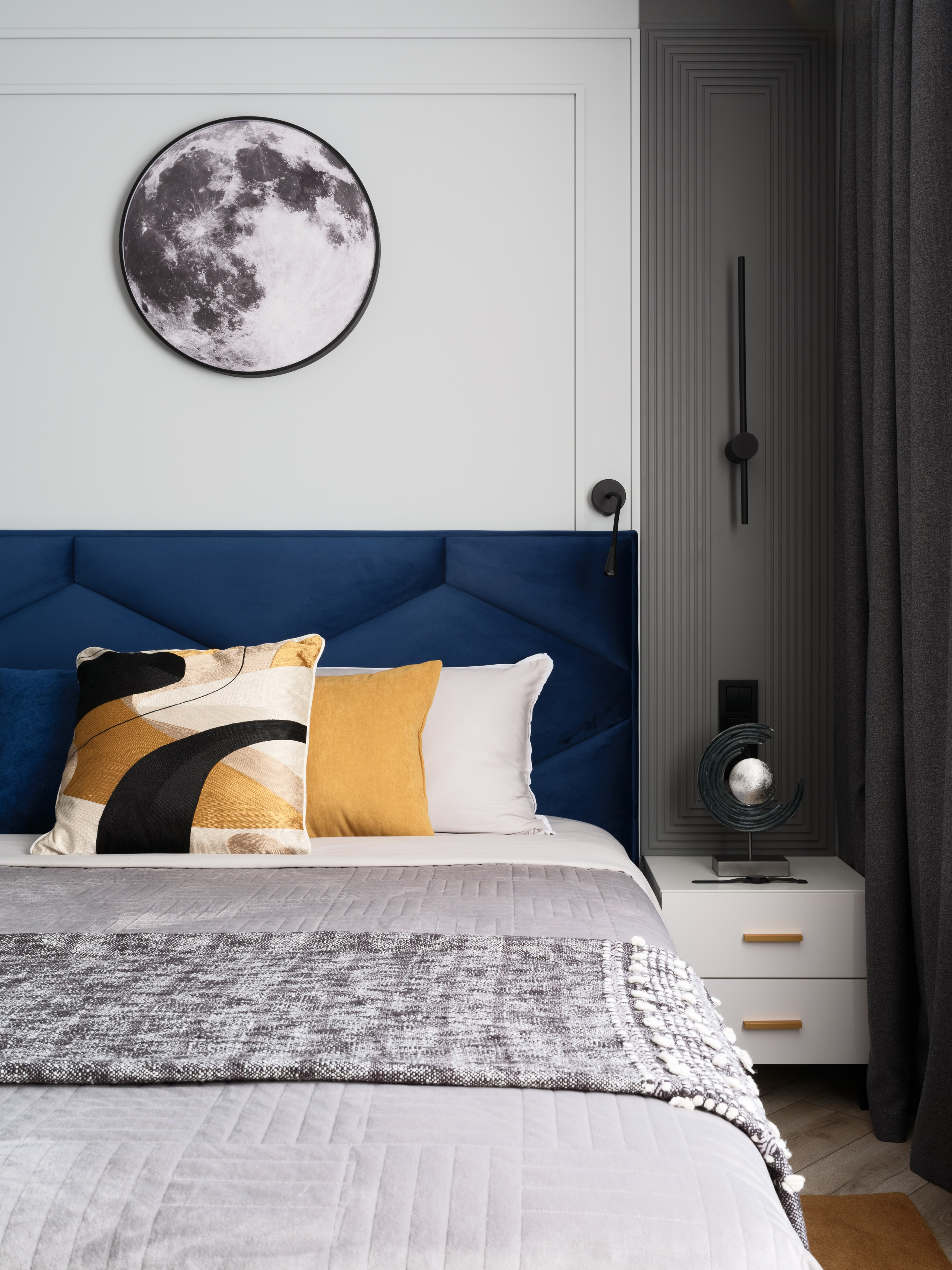 Дизайн спальни с акцентом на изголовье кровати насыщенного синего оттенка, декоративные подушки в чёрно-бело-золотой гамме и картина Луны на стене. Интерьер разработан дизайнером Евгенией Ермошиной, съёмка выполнена Сергеем Денисенко.