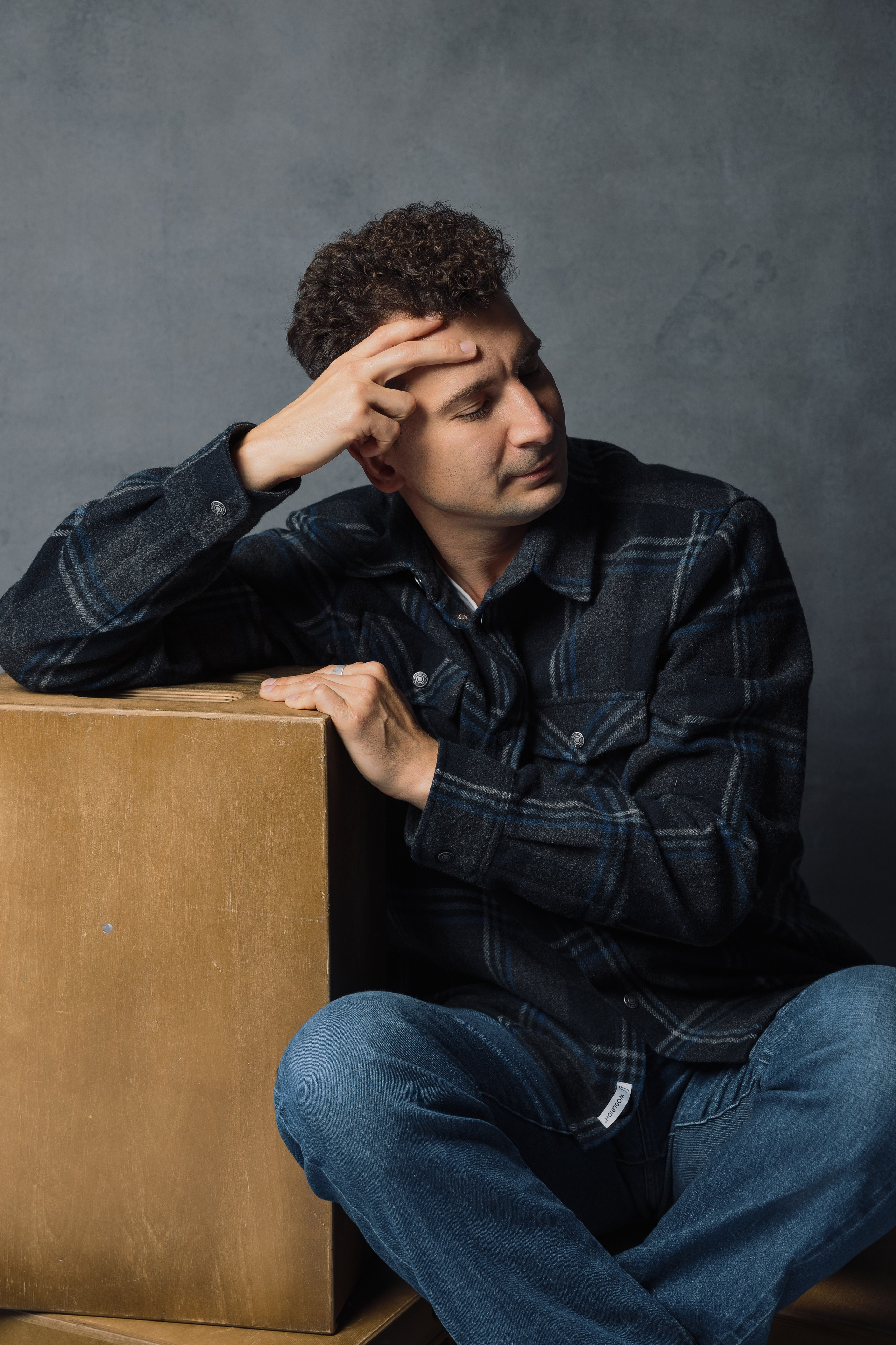 Портретная фотография мужчины в джинсах и клетчатой рубашке на сером фоне