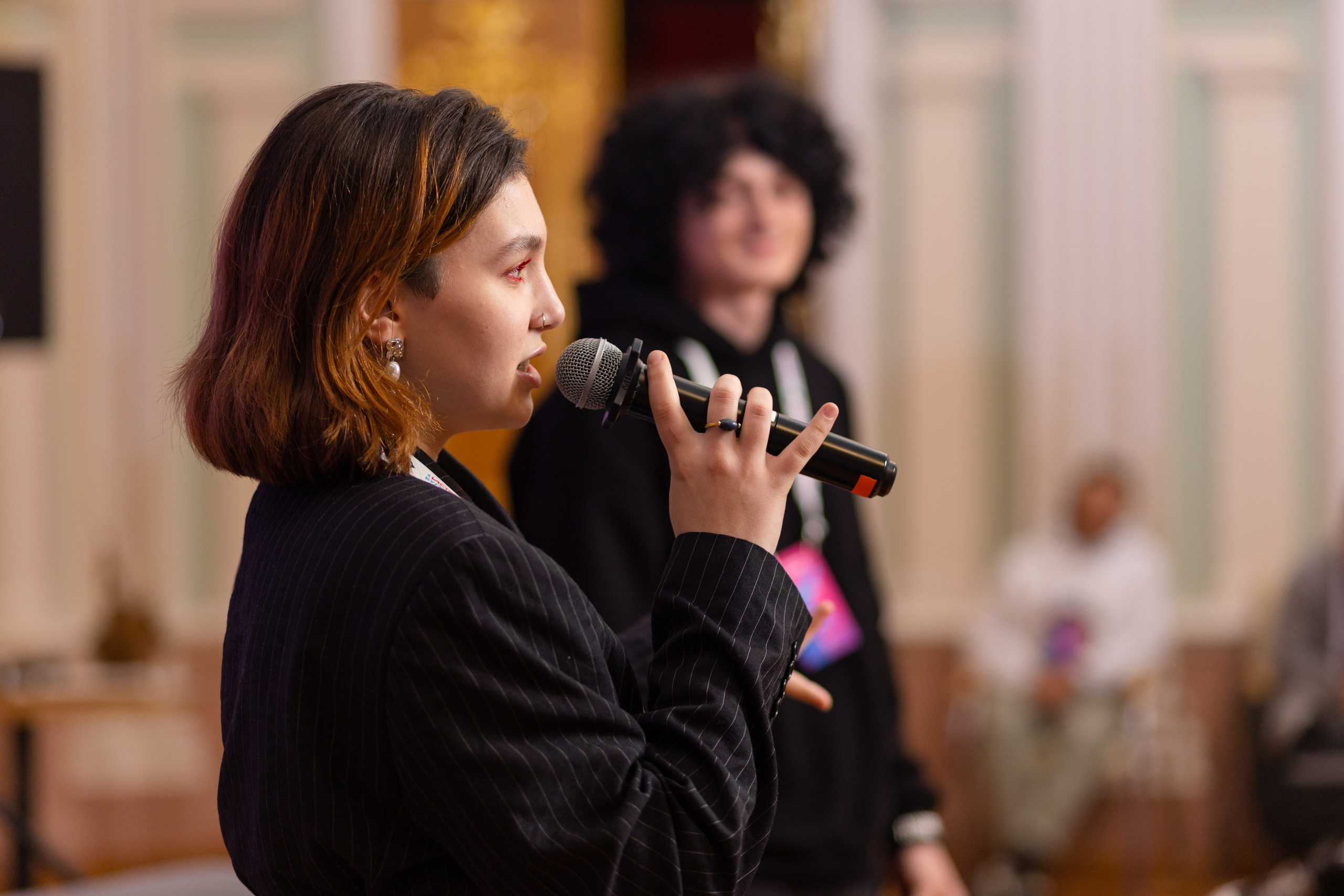 Девушка в профиль с микрофоном на переднем плане.