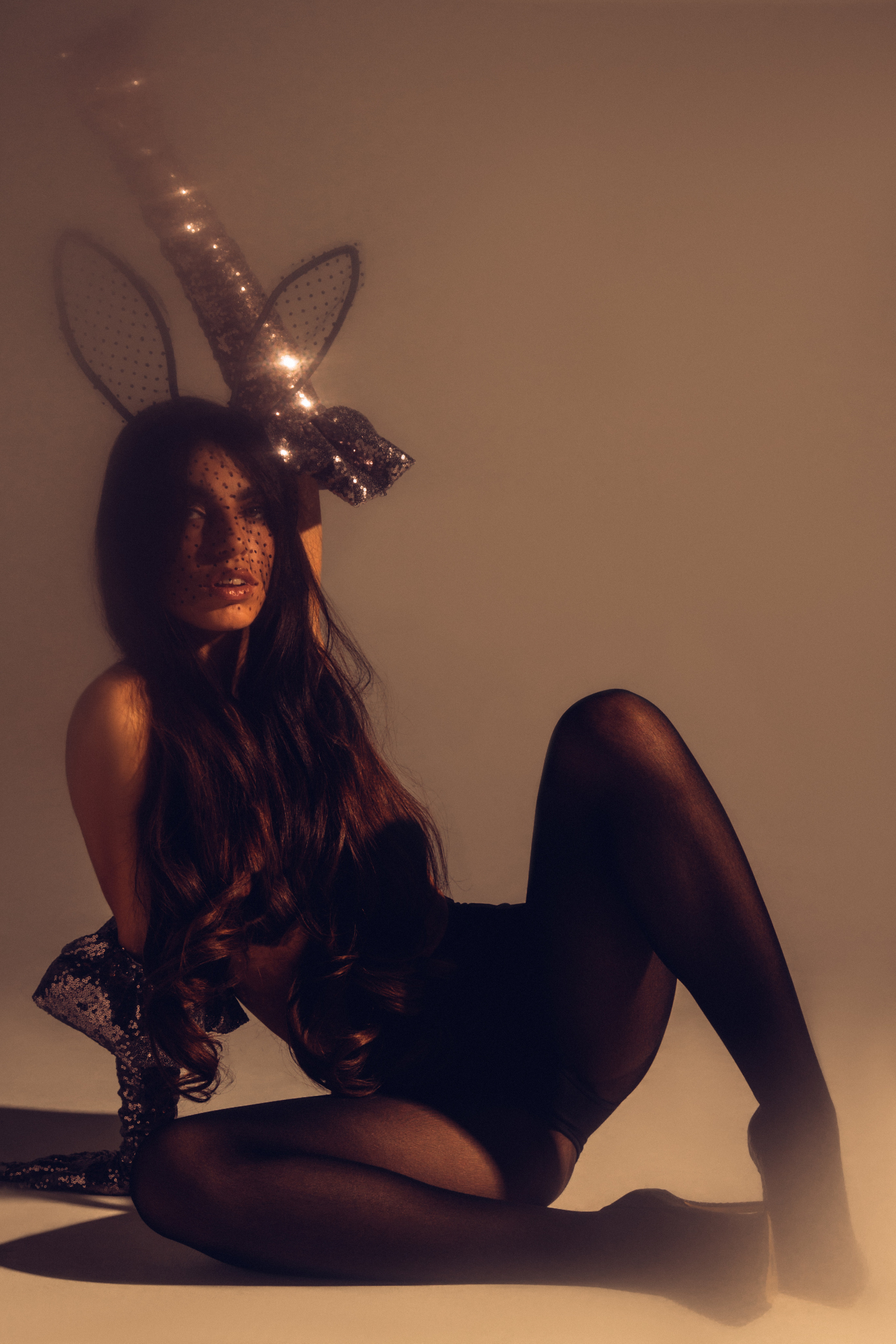 сексуальная девушка на полу в приглушенном свете в черных колготках и с маской на лице