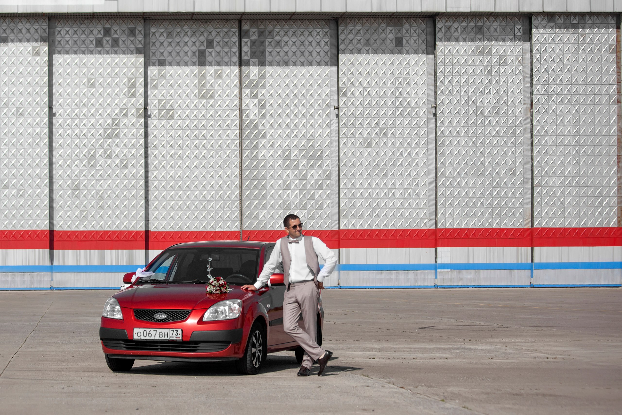 Жених у красной машины на фоне металлической стены аэропорта в городе Ульяновск