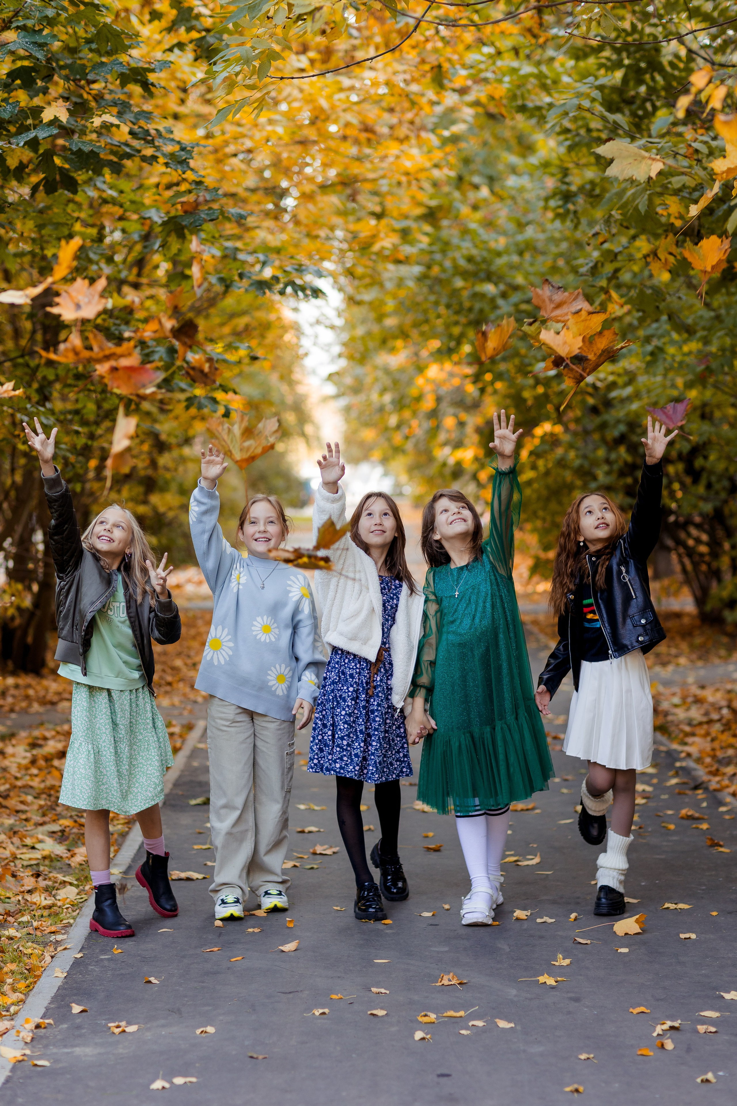 Девочки подружки подкидывают листья в парке осенью