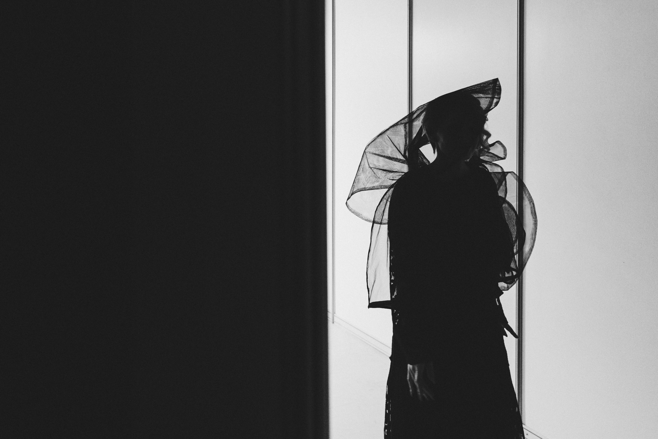 силуэт дамы в шляпе и вуали на фоне белой стены