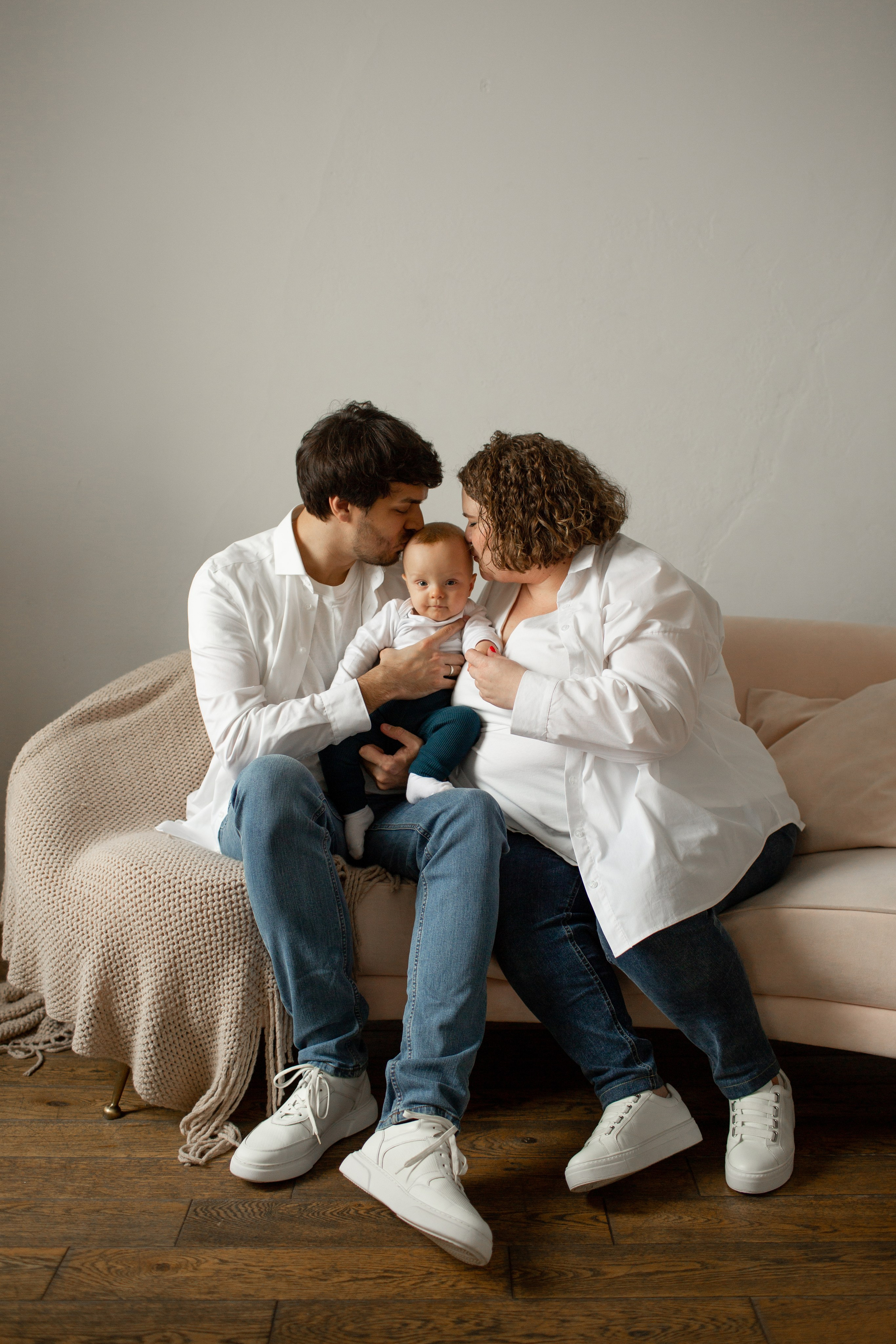 Семейный портрет в фотостудии: родители целуют ребенка.