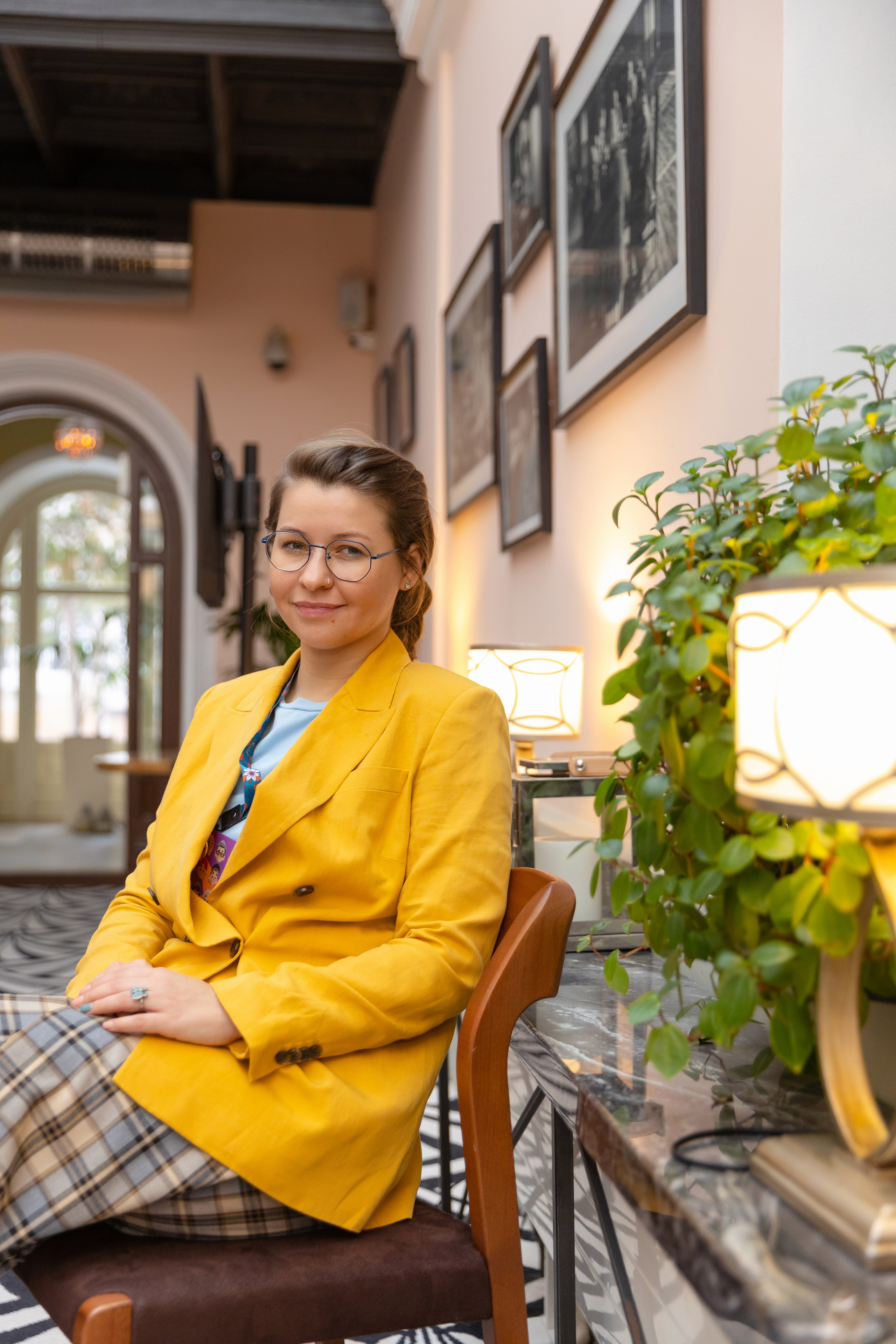 Ведущая Чемпионата сидит у стены заполненную фотографиями в рамках.