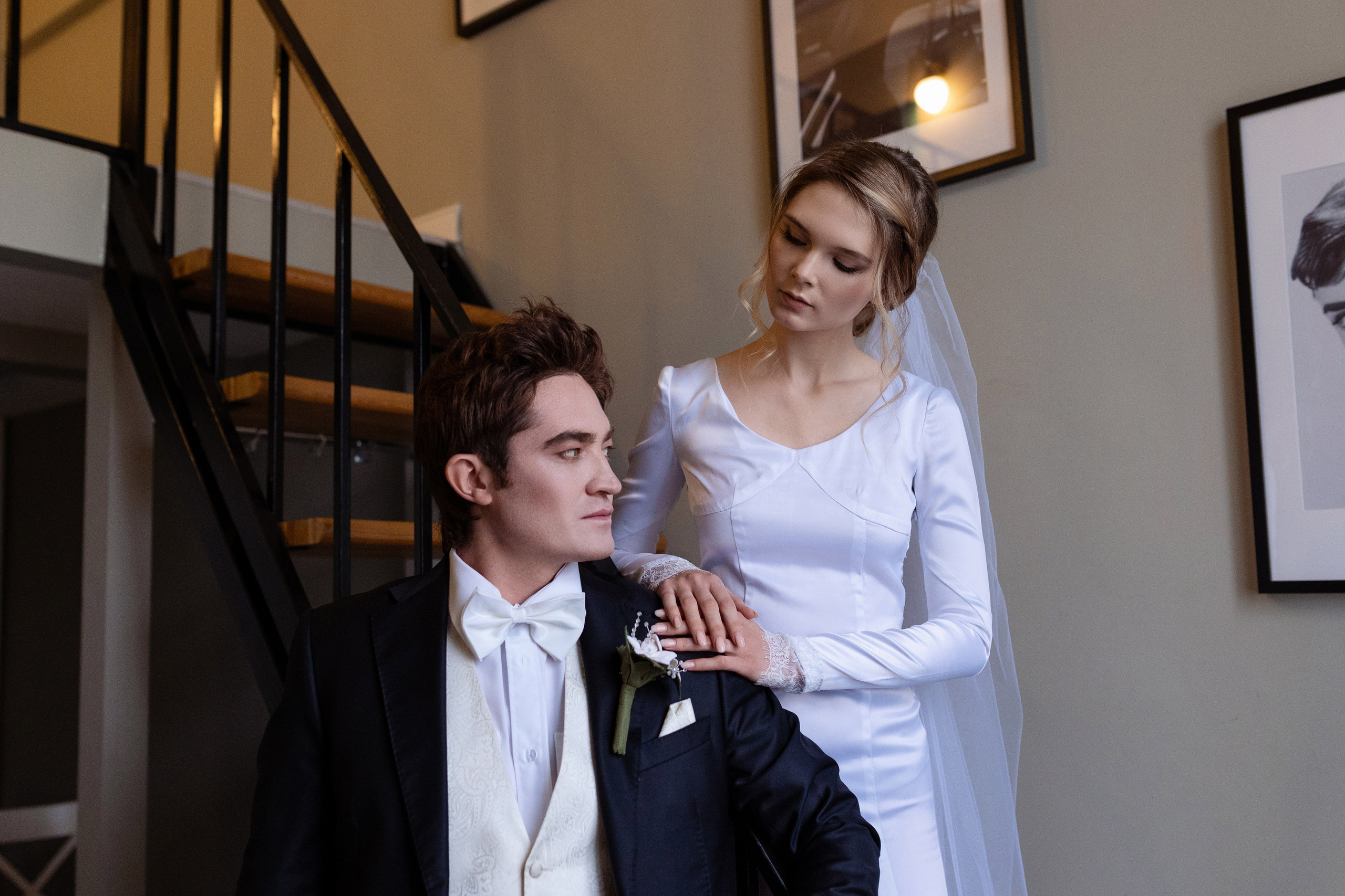 Невеста стоит на лестнице за спиной жениха, положив руки на его плечо.