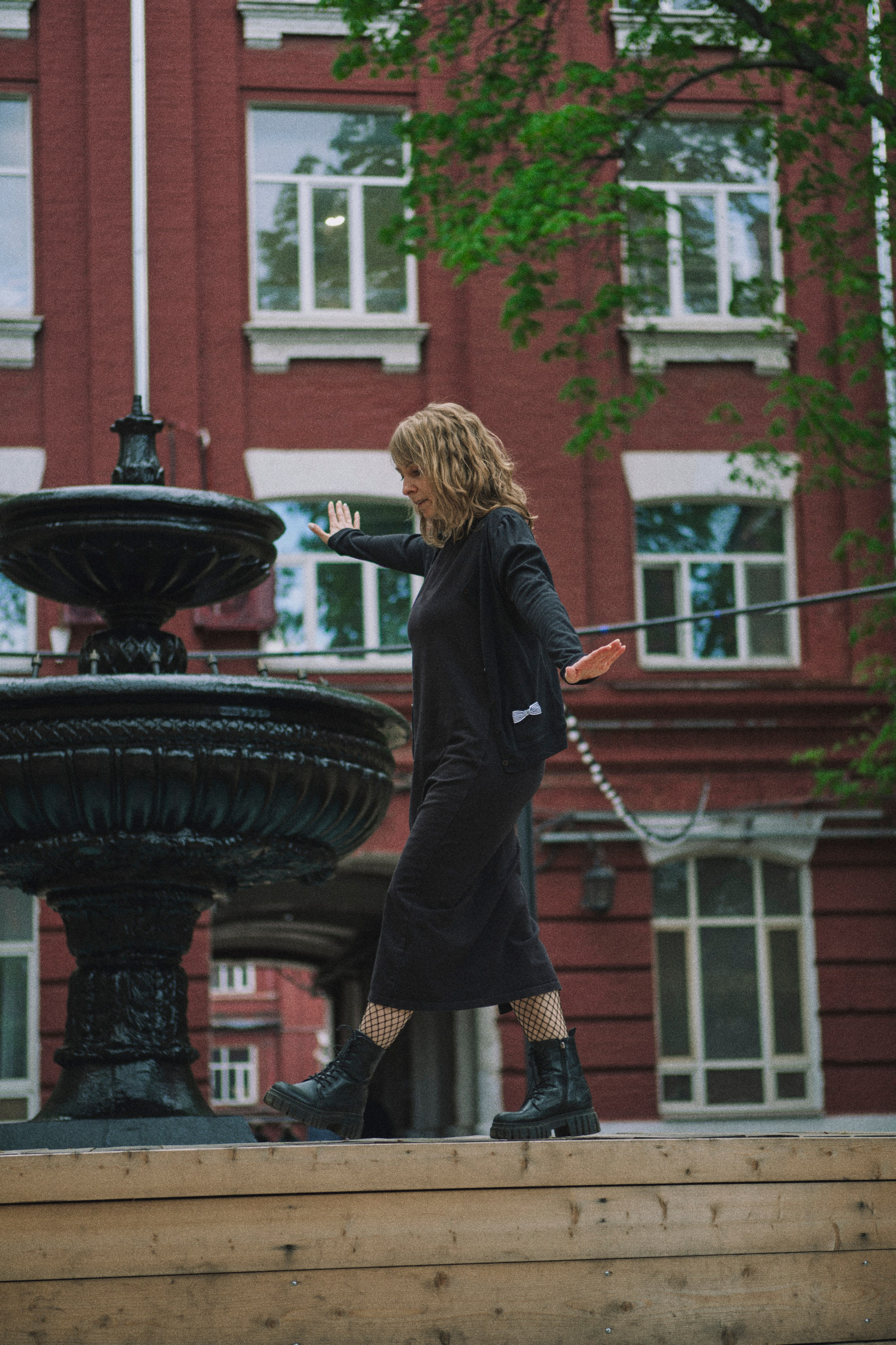 Женщина идет вдоль фонтана по бортику, ловя баланс