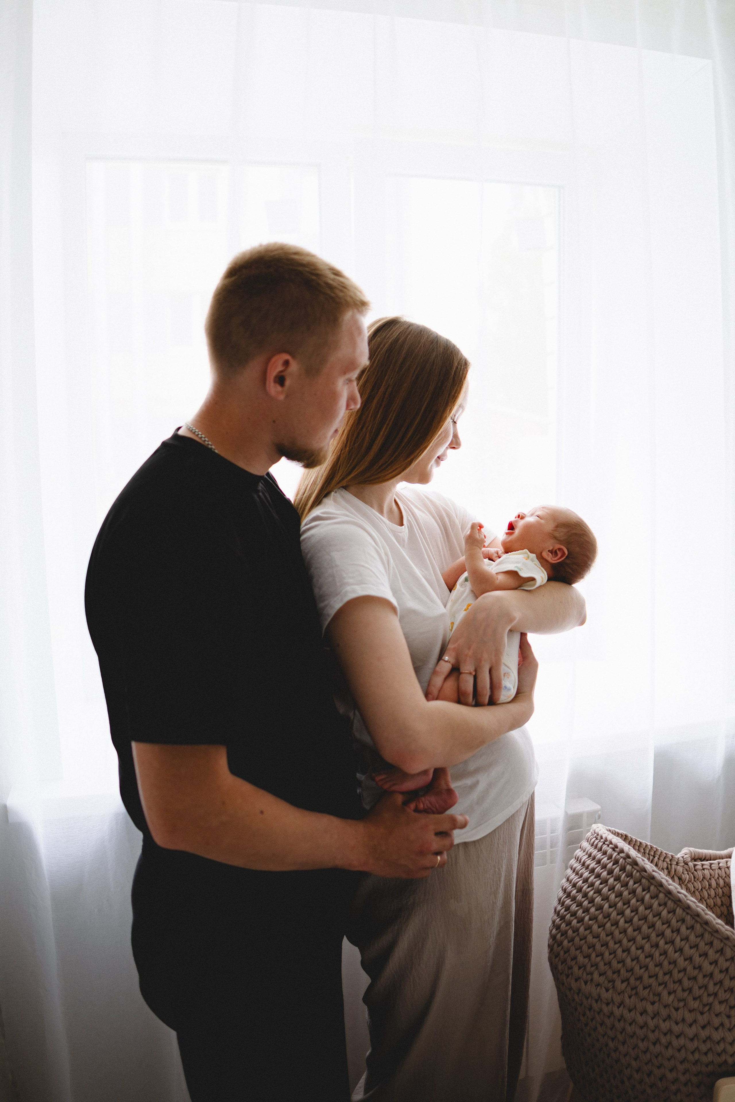 Parents standing by the window with their newborn baby