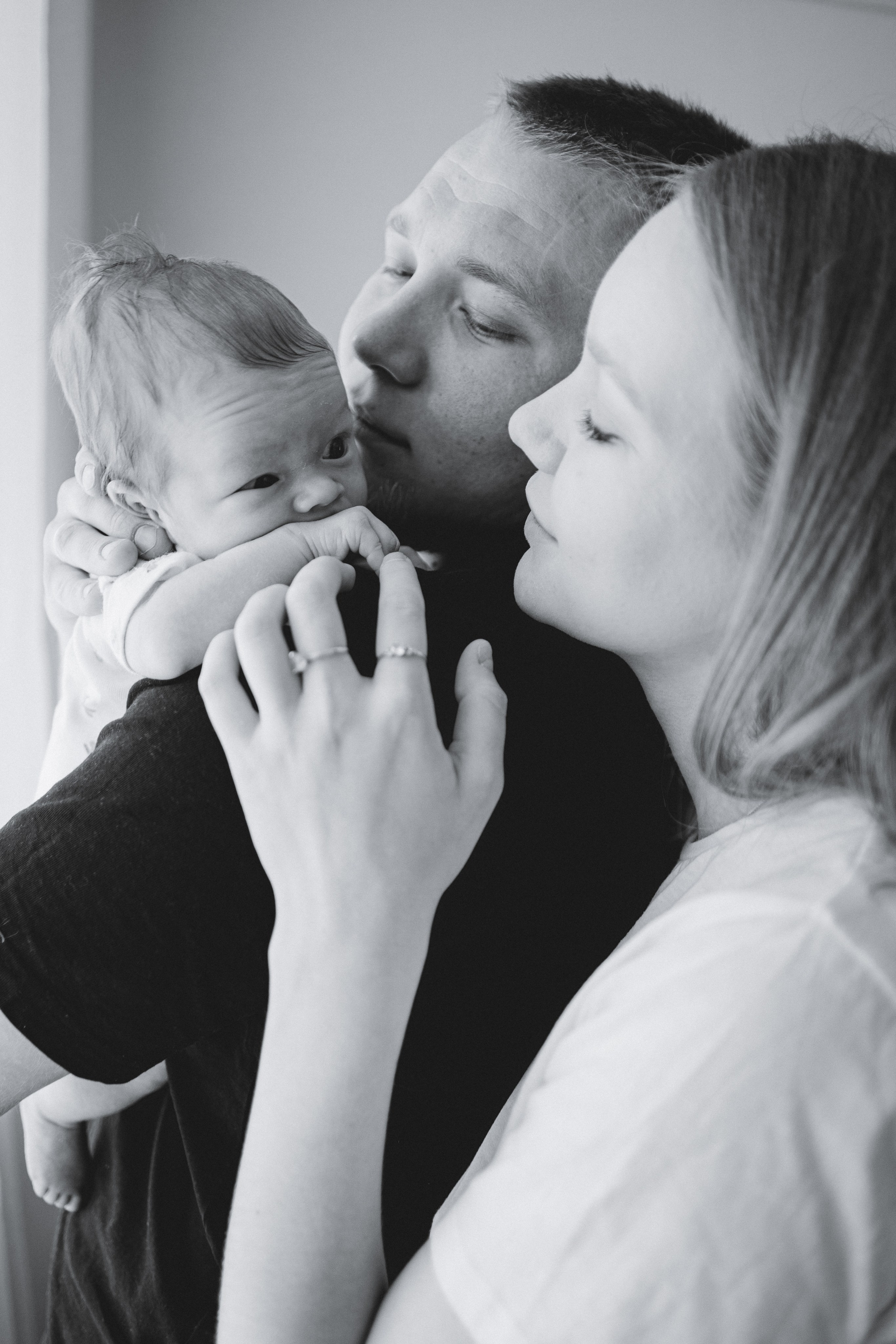 Parents kissing their newborn in a black-and-white portrait