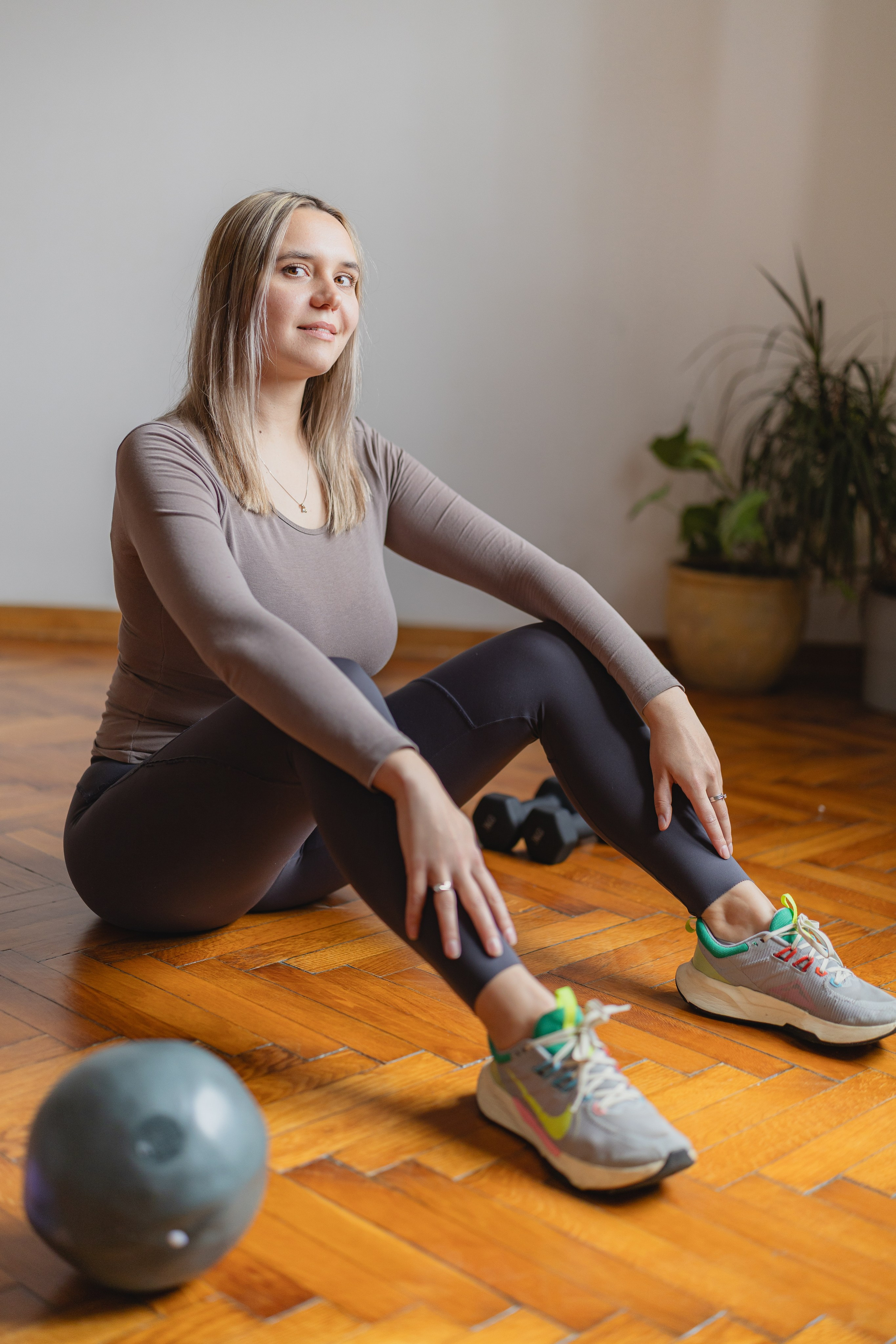 A portrait of a cheerful young woman smiling directly into the camera next to workout gear
