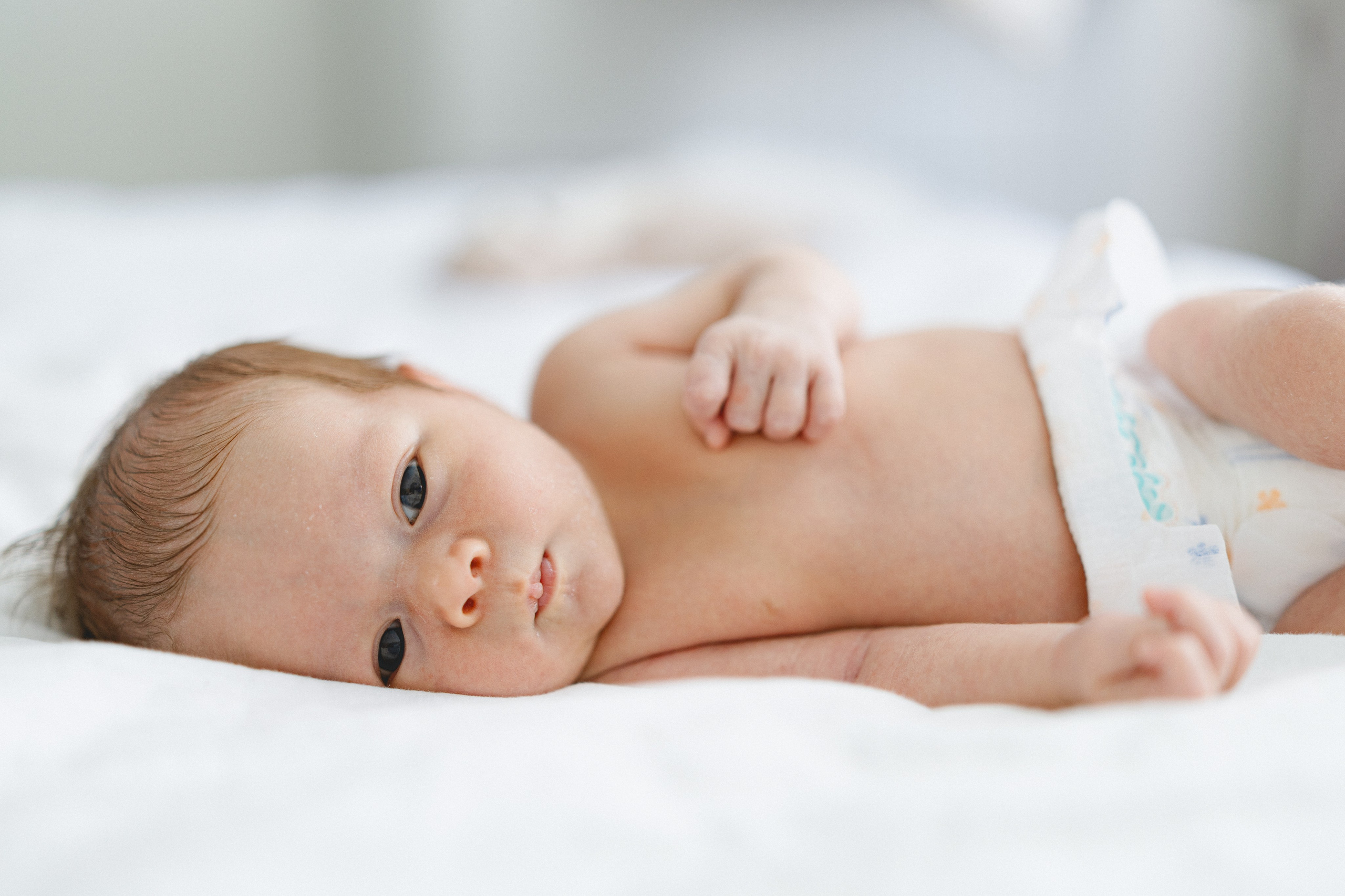 Awake newborn baby resting on a white bed