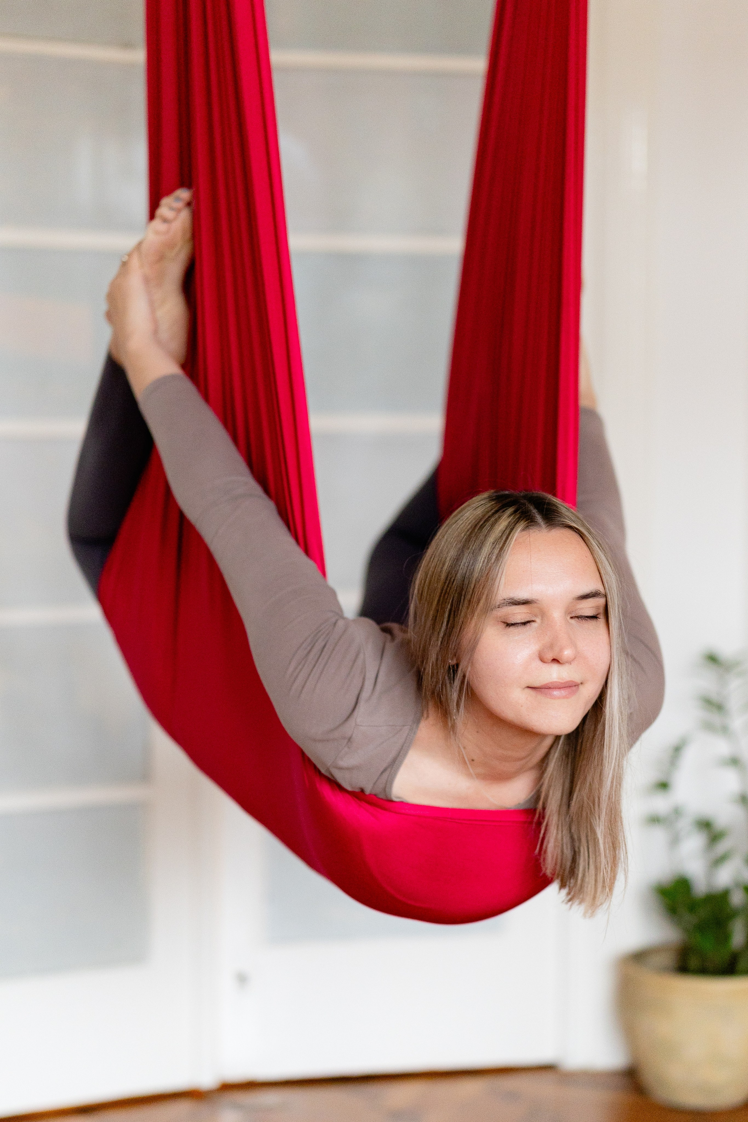 A smiling girl sitting inside a red hammock swing during an aerial fitness class