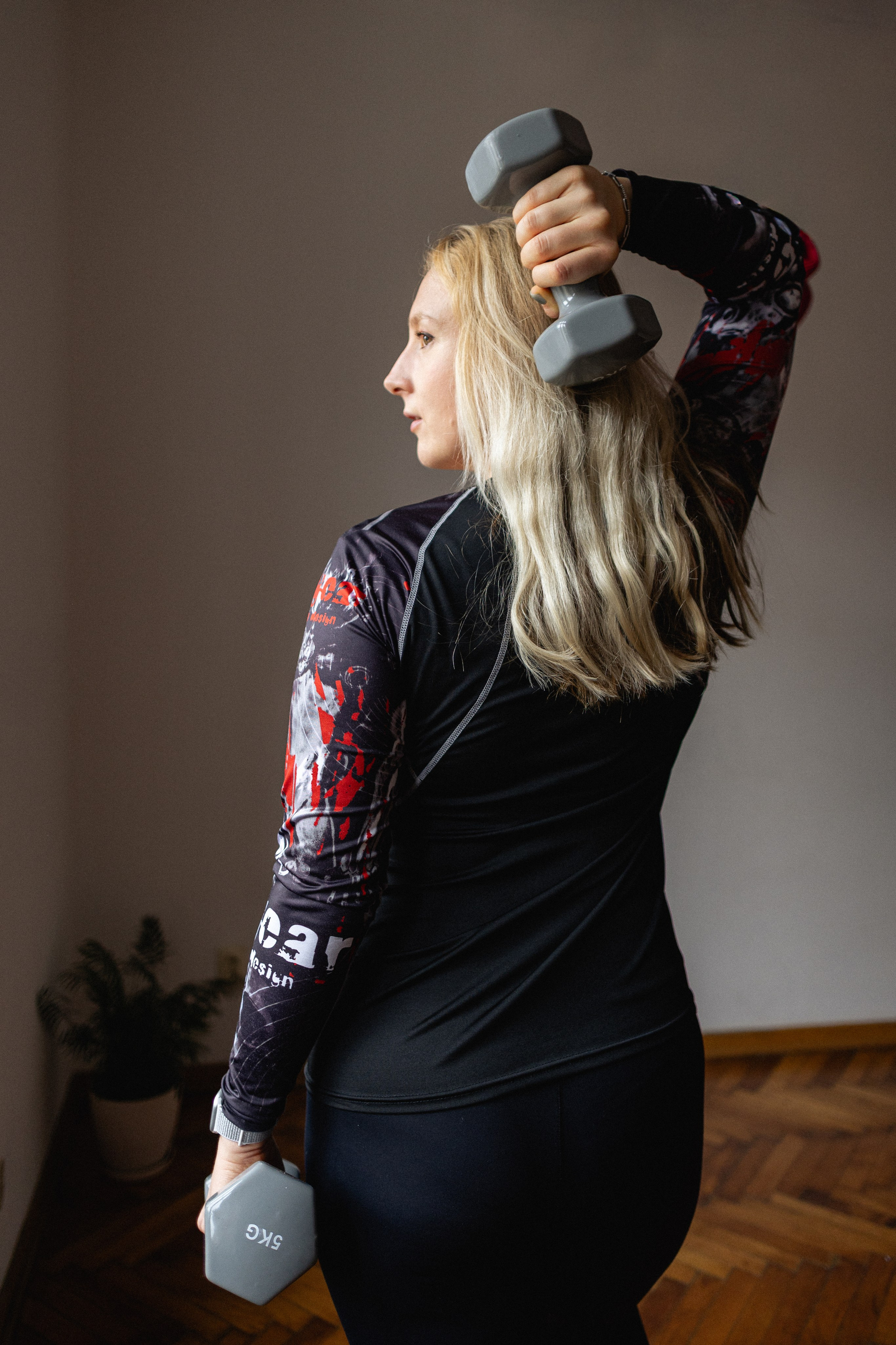 A woman training her upper body and shoulders with light dumbbells in a home-style studio room