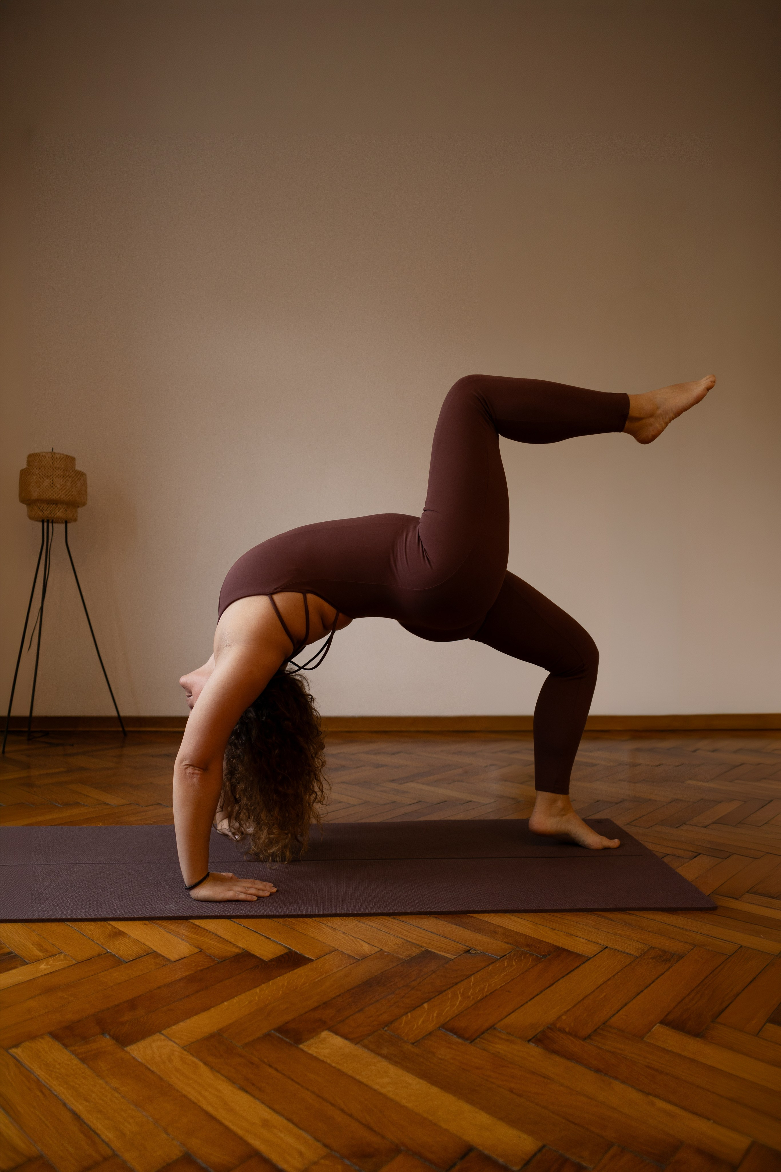 A practitioner performing a one-legged wheel bridge pose on a dark yoga mat