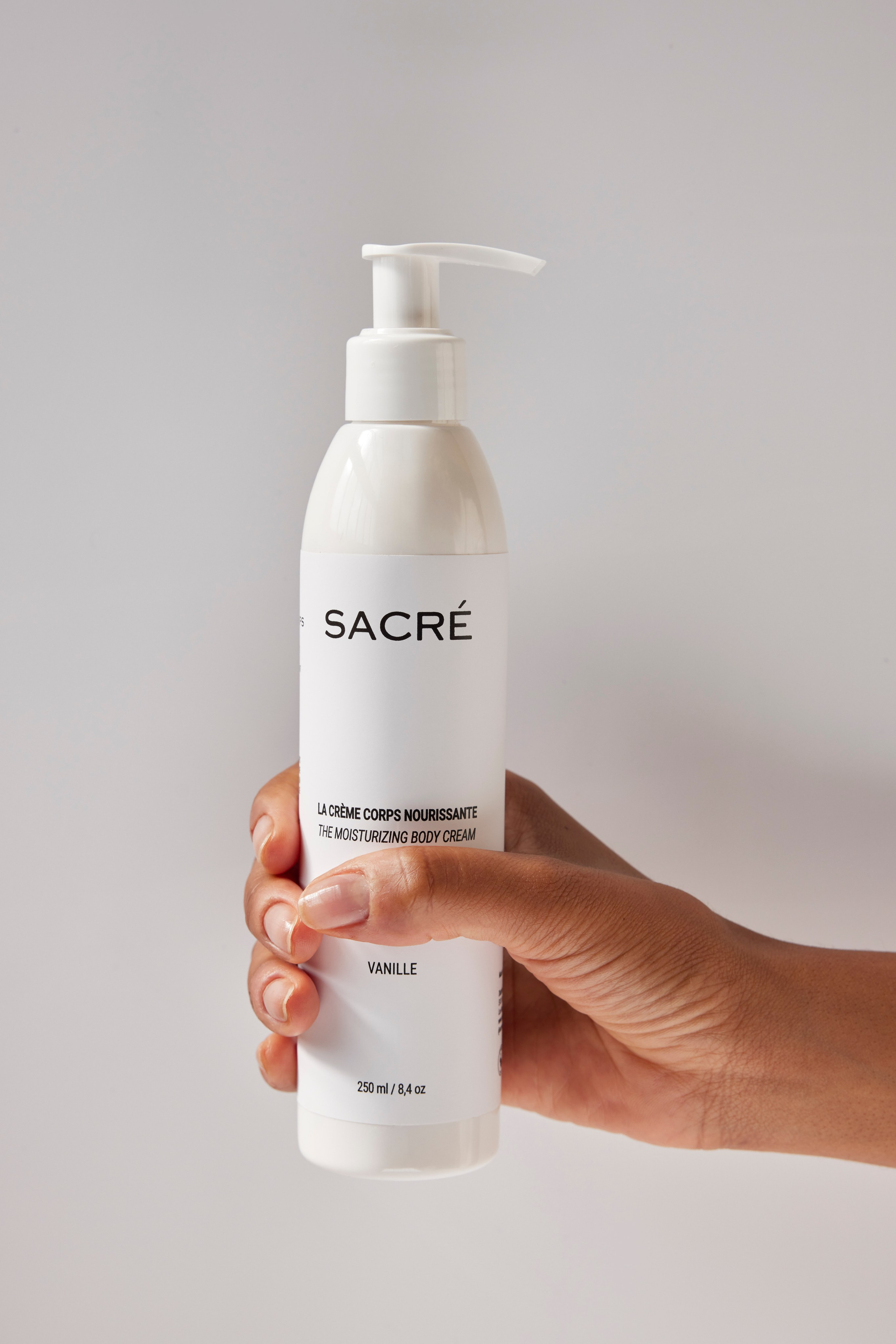 Hand holding a white bottle of lotion against a neutral background, highlighting branding simplicity.