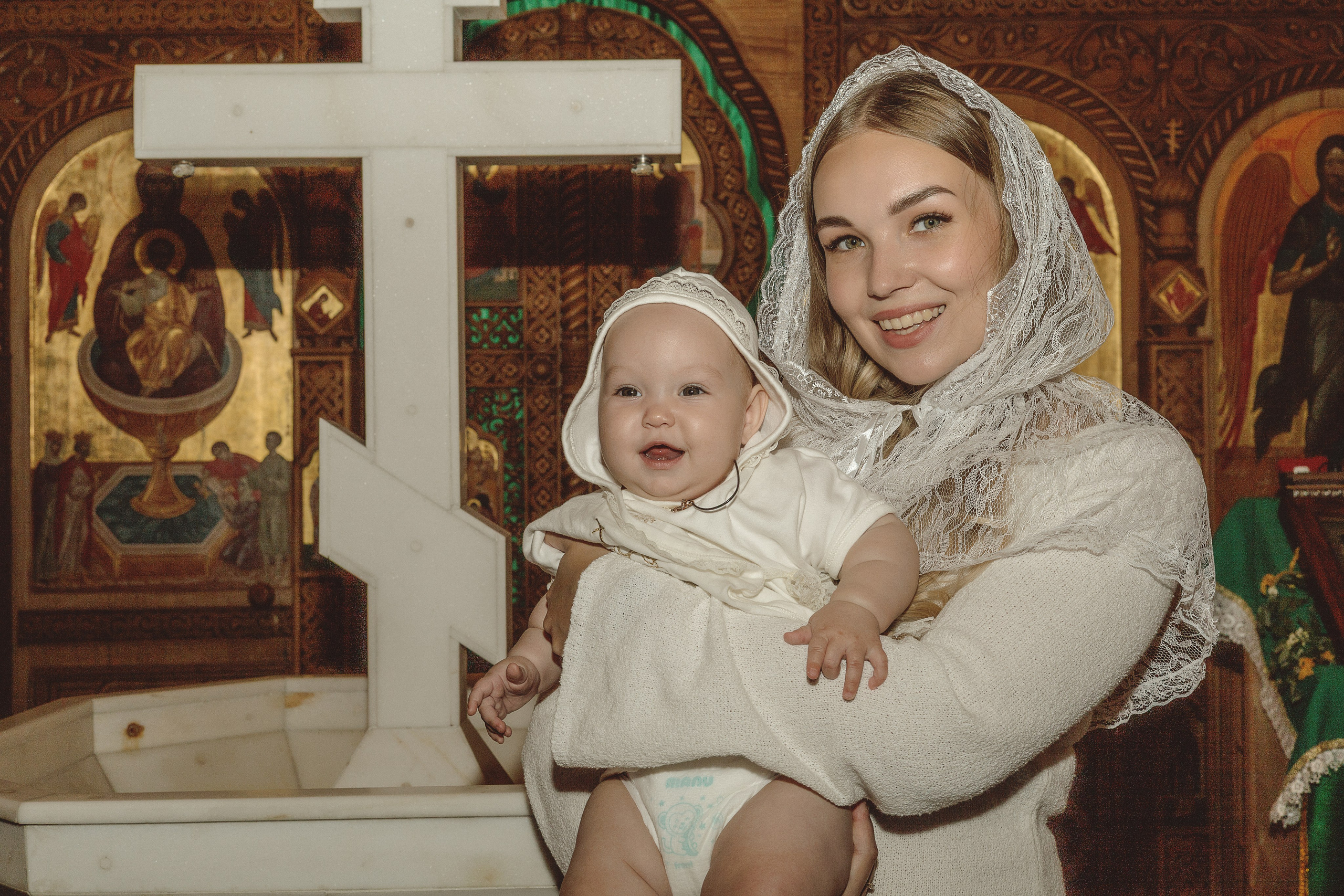портрет в храме после крещения - мама держит маленькую дочку на руках, рядом распятие