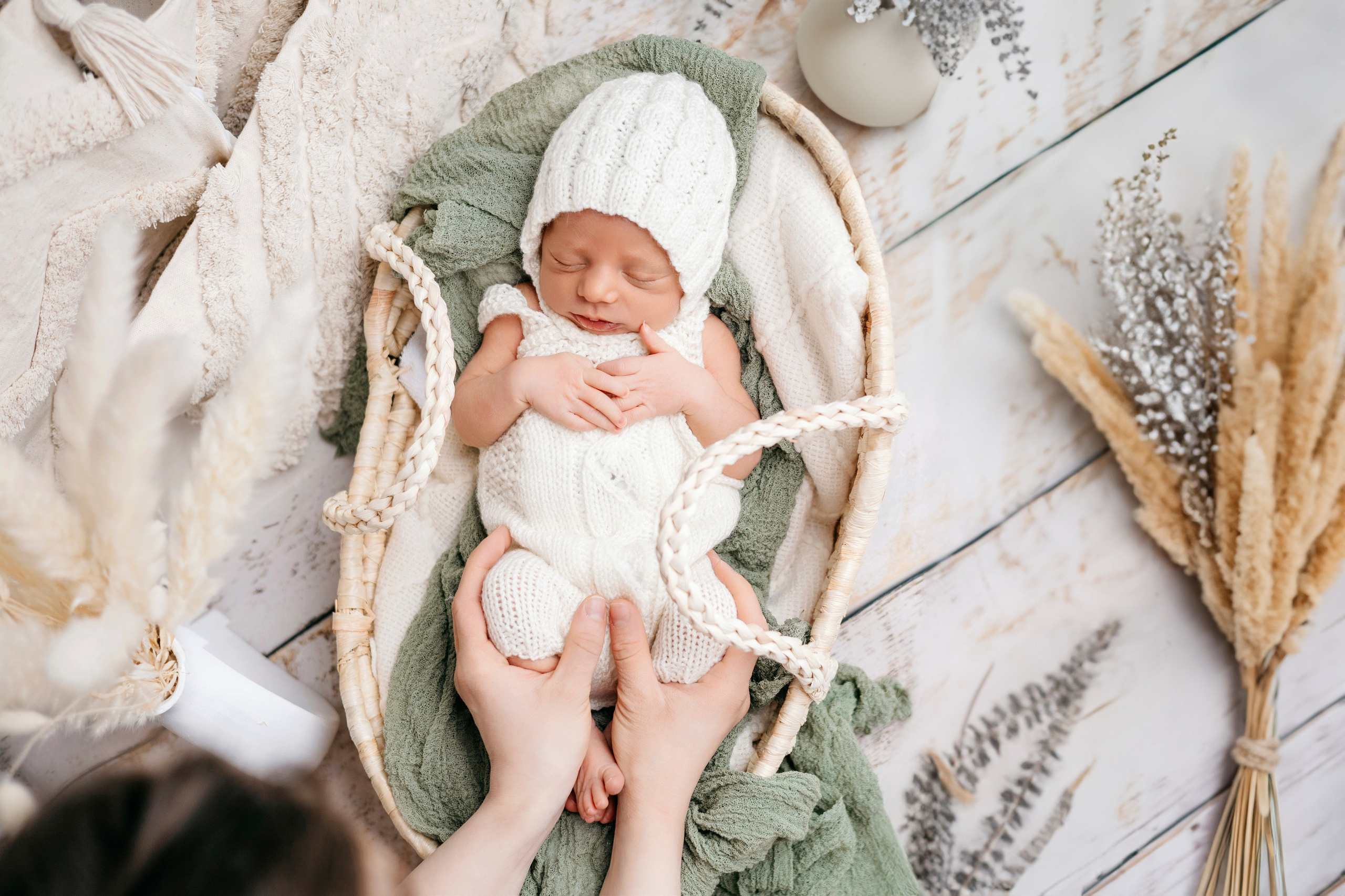 Новорожденный в корзине с тканями землистых тонов, окруженный сухими цветами и хлопком и колосками