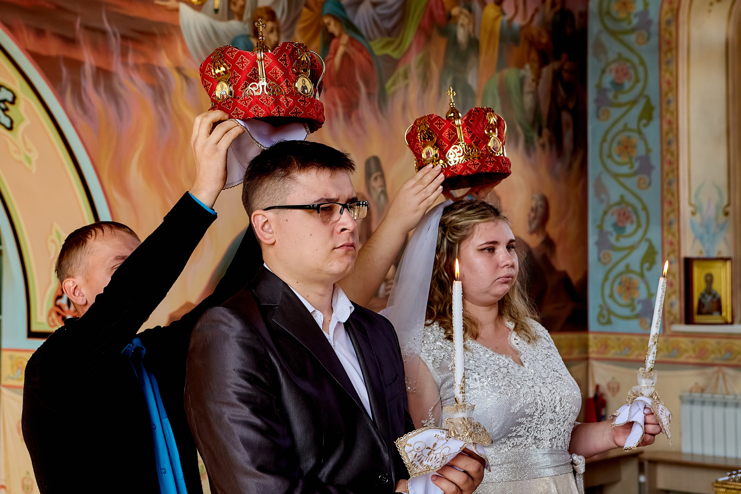 Свидетели над главами у молодых держат венцы. Молодые стоят со свечами