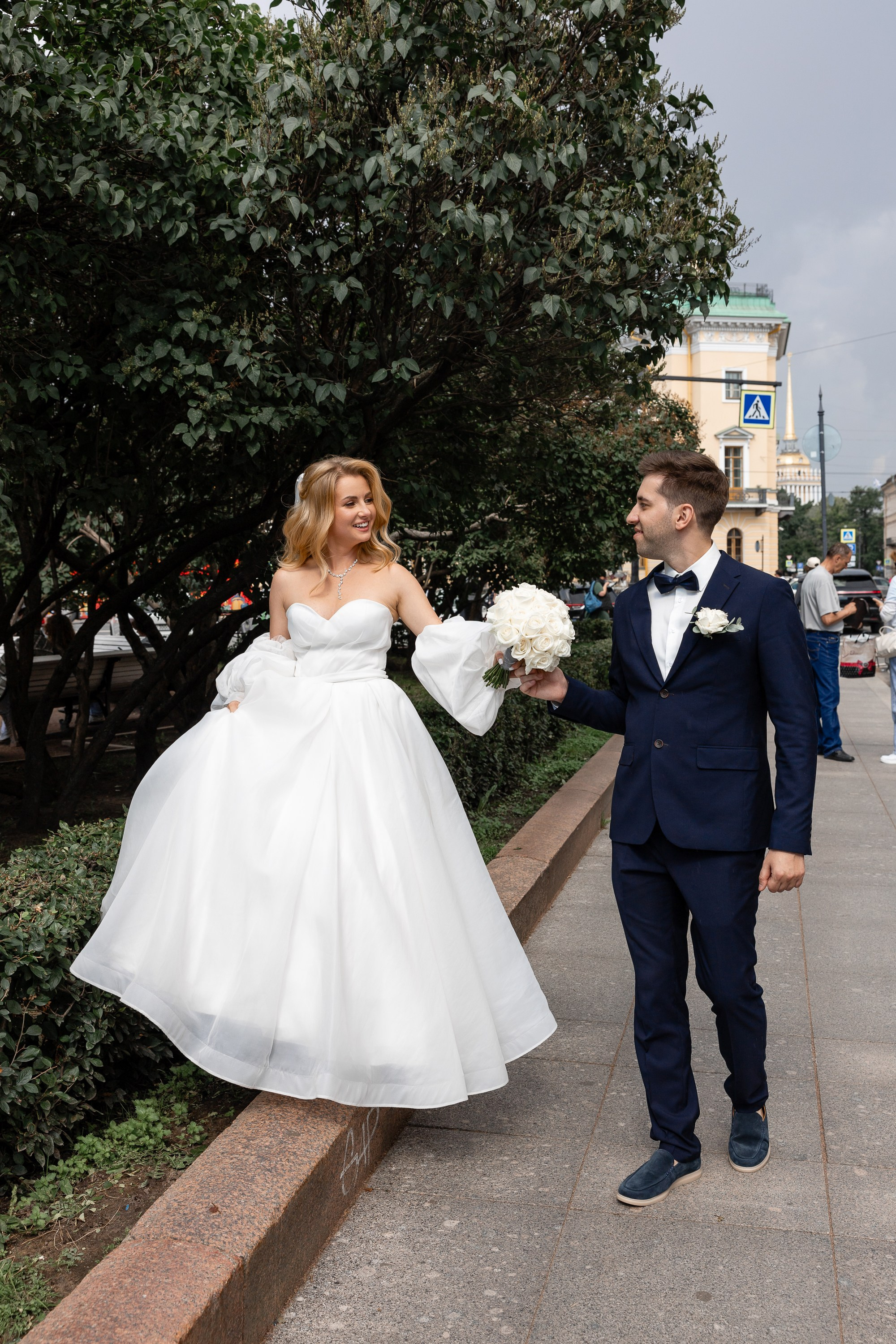 Невеста идет по бортику Исаакиевского сквера, а жених поддерживает ее за руку