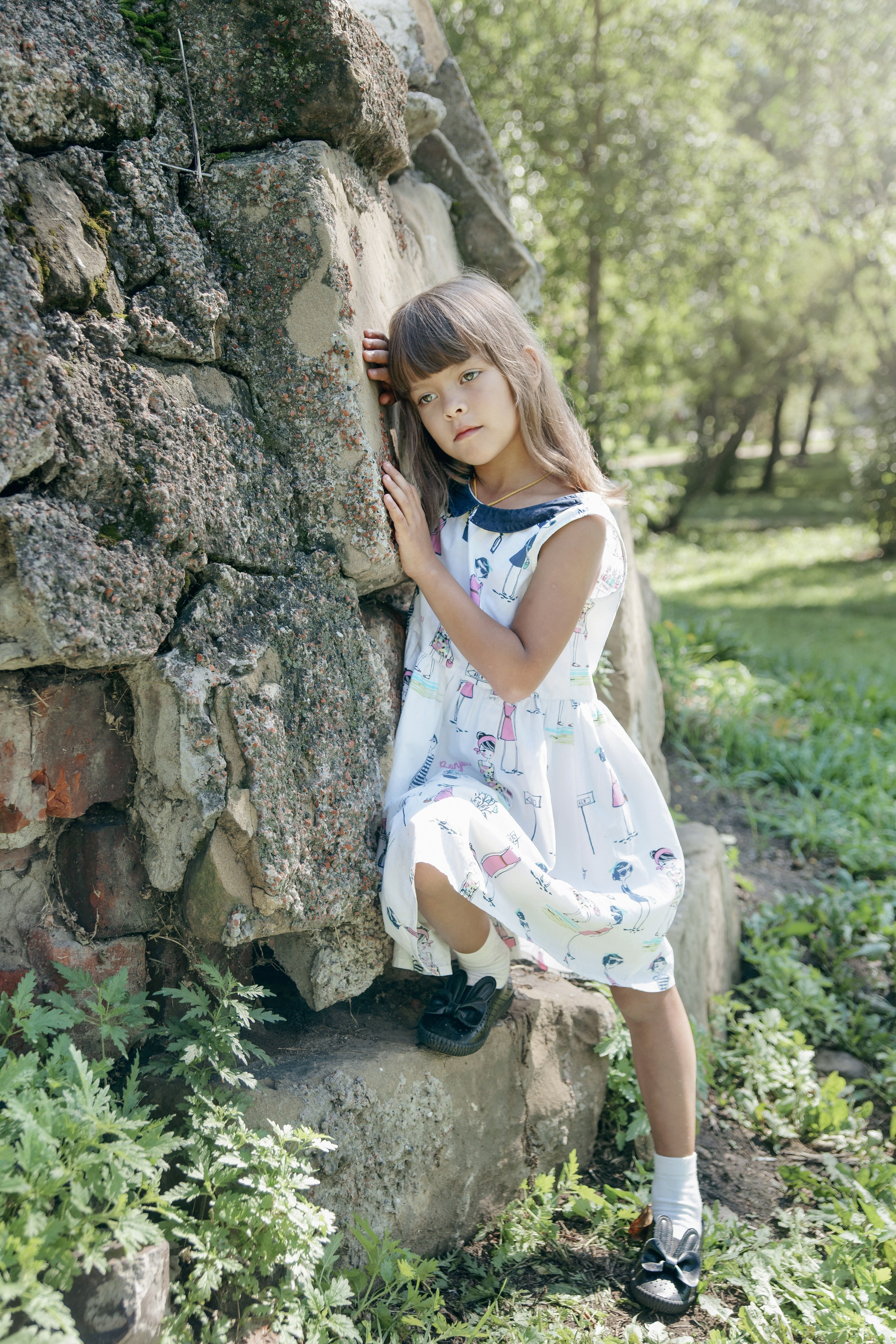 Детская фотосессия летом - девочка стоя у каменной стены