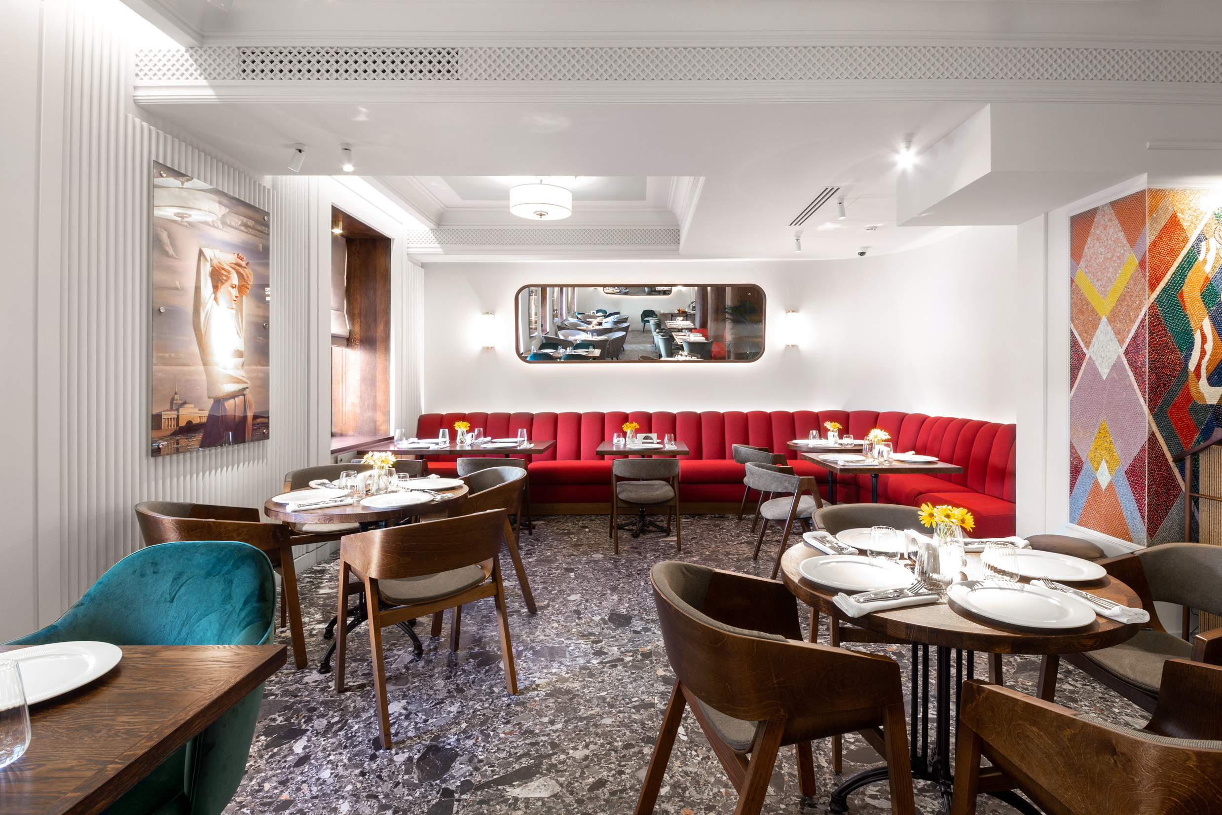 Зал ресторана с мозаикой в советском стиле на стенах. Красный диван и удобные стулья.