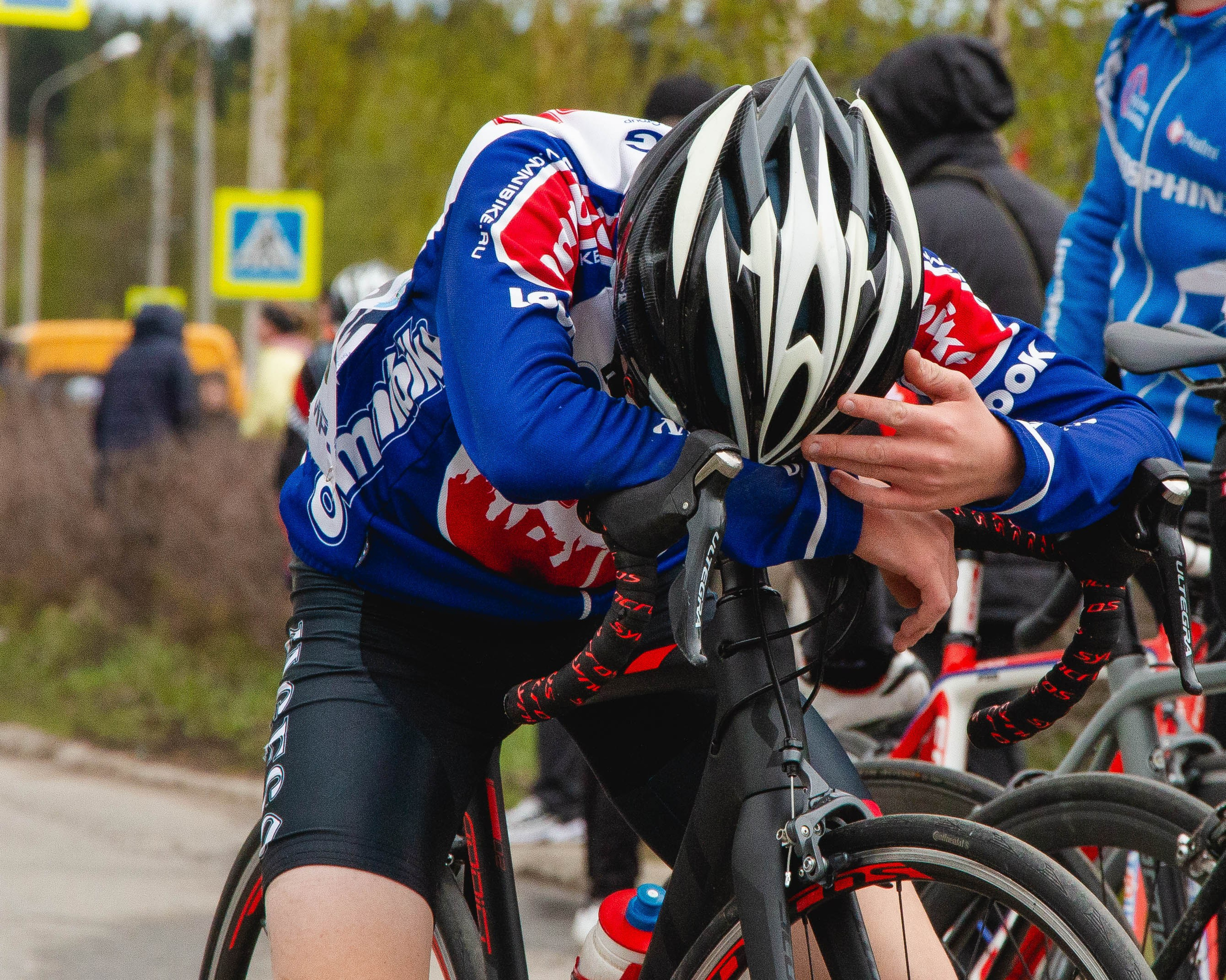 Уставший велосипедист стоит опустивши голову на руль после финиша