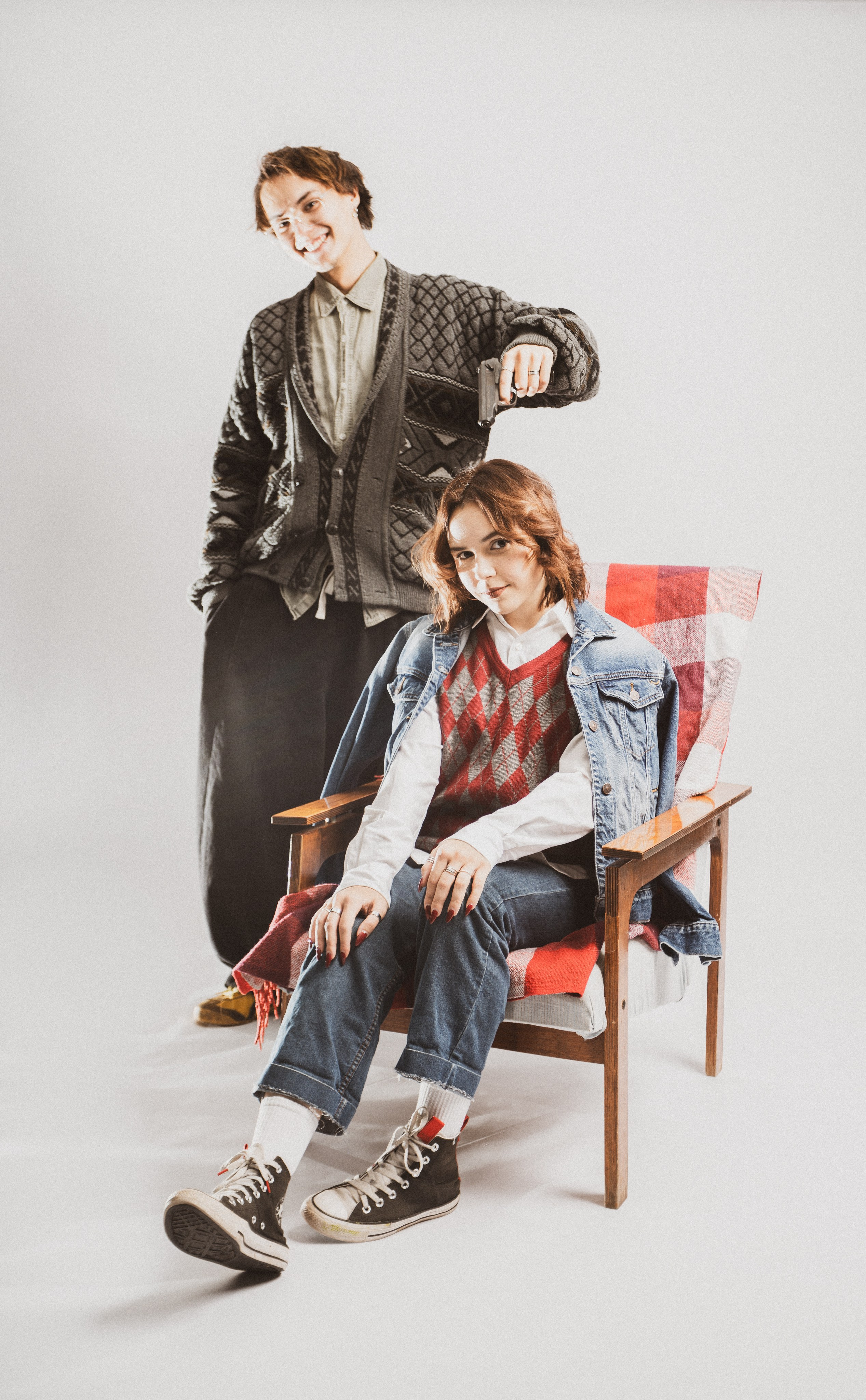 Девушка в черной куртке и джинсах сидит на стуле в студийном свете.