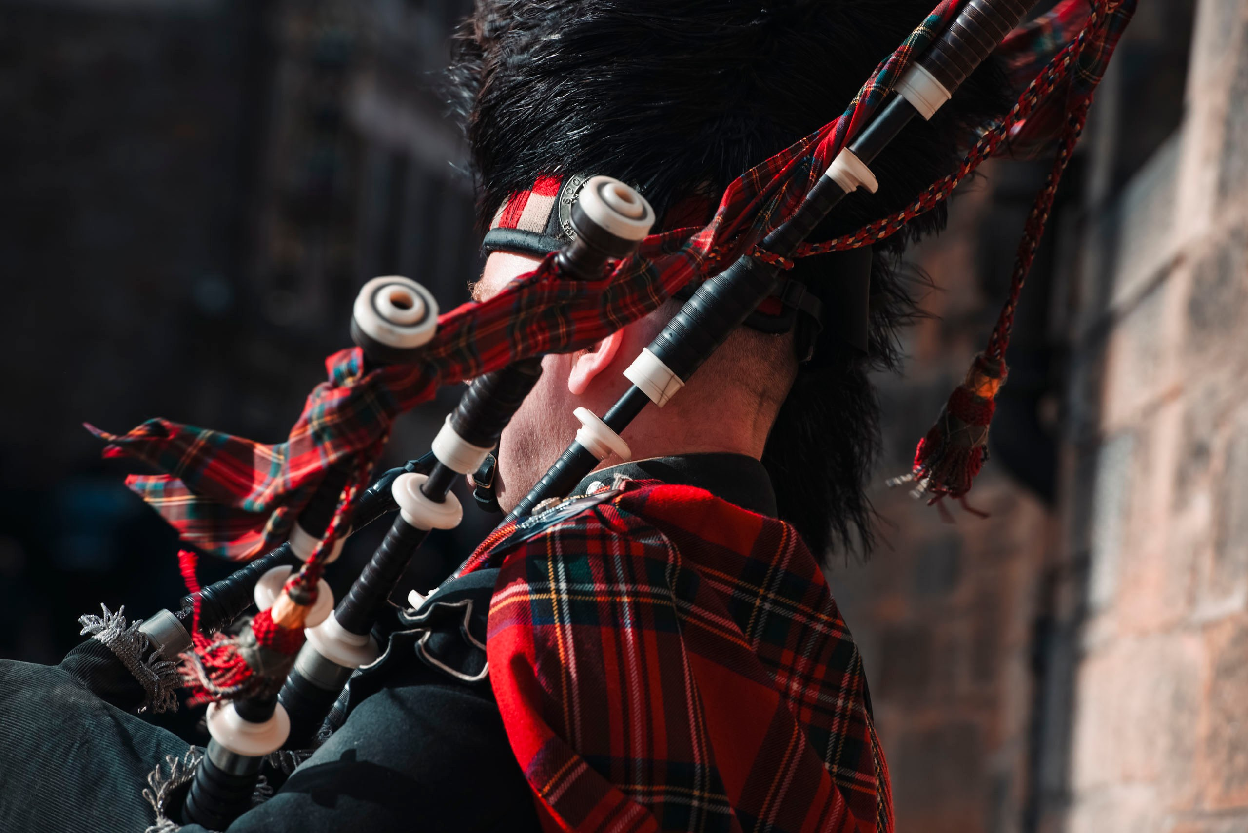 *Шотландский волынщик в традиционном красном тартане играет на Большой горной волынке (Great Highland Bagpipe) на улице Эдинбург.