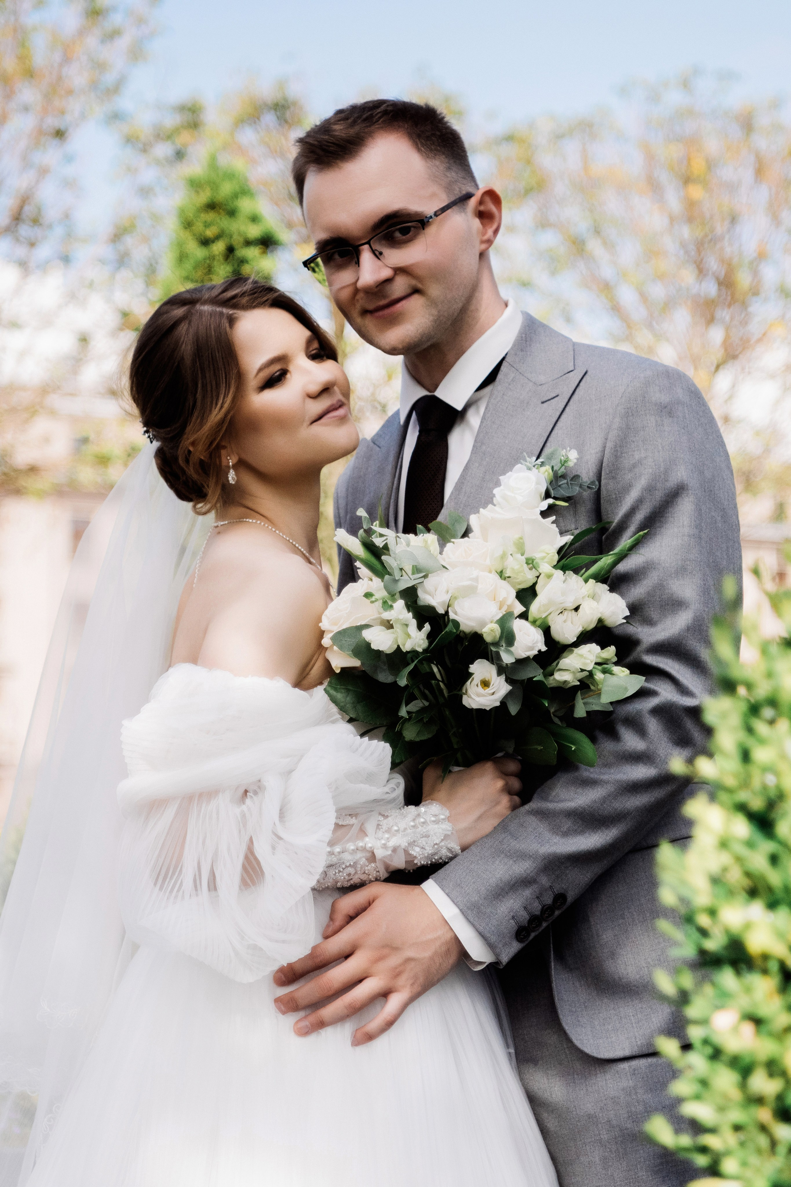 Невеста и жених обнимаются в саду — свадебный портрет на открытом воздухе