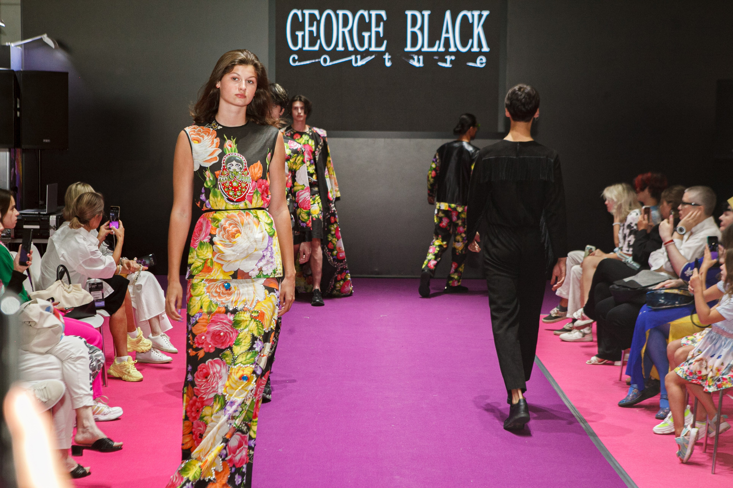  "Модели в ярких нарядах проходят по подиуму во время показа мод, освещенные яркими софитами и окруженные восторженными зрителями."