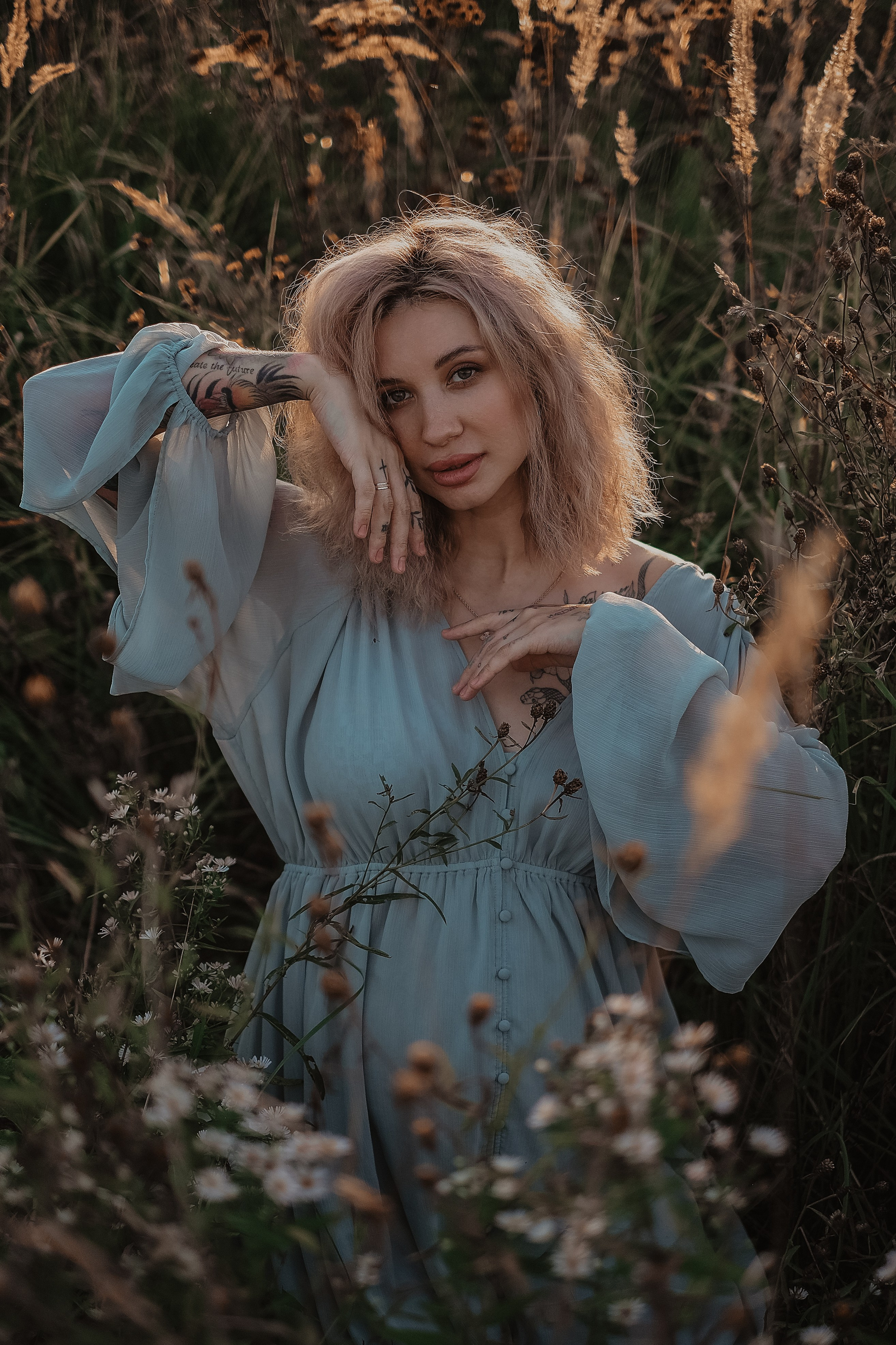 Портрет беременной девушки в голубом платье в поле на закате в окружении цветов и трав