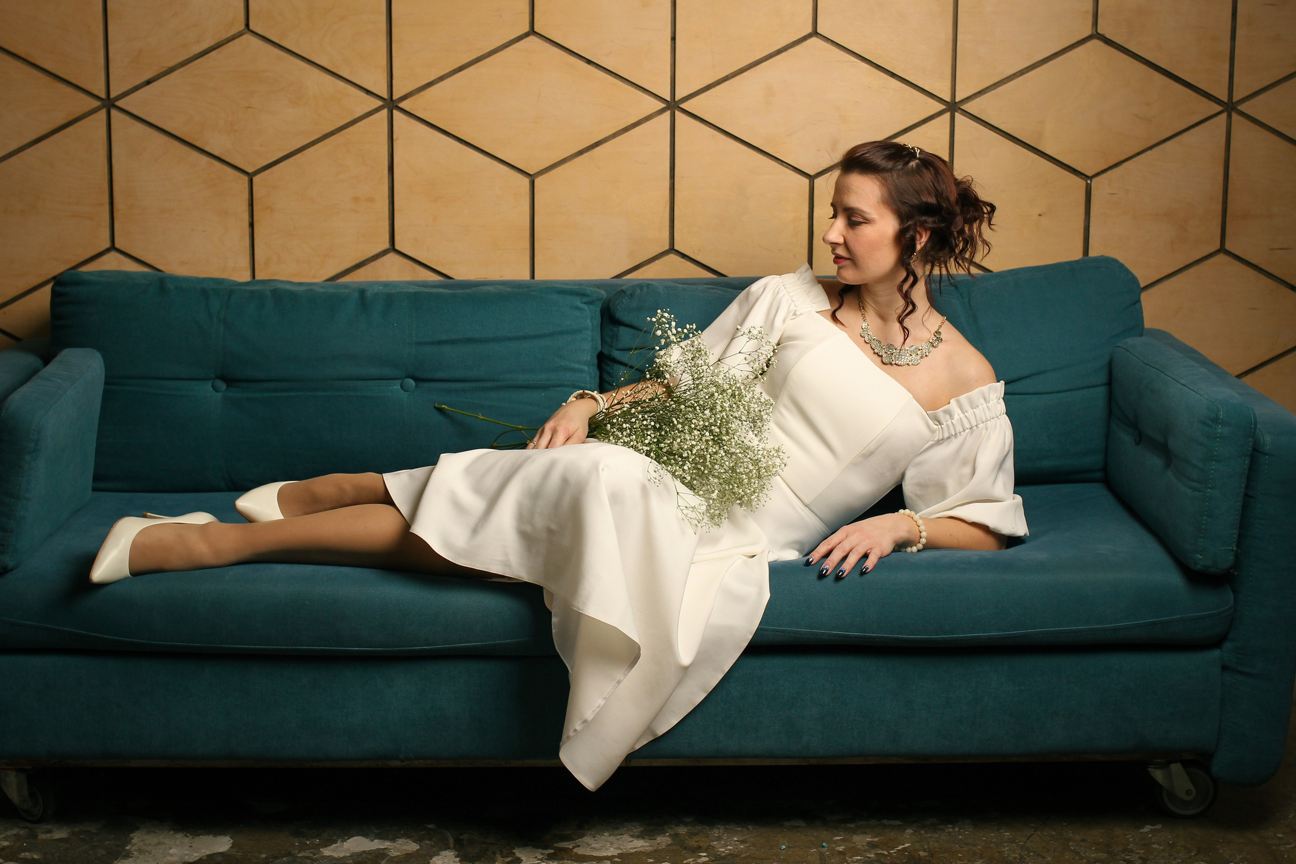 Художественный портрет девушки в белом платье с цветами на диване в студии