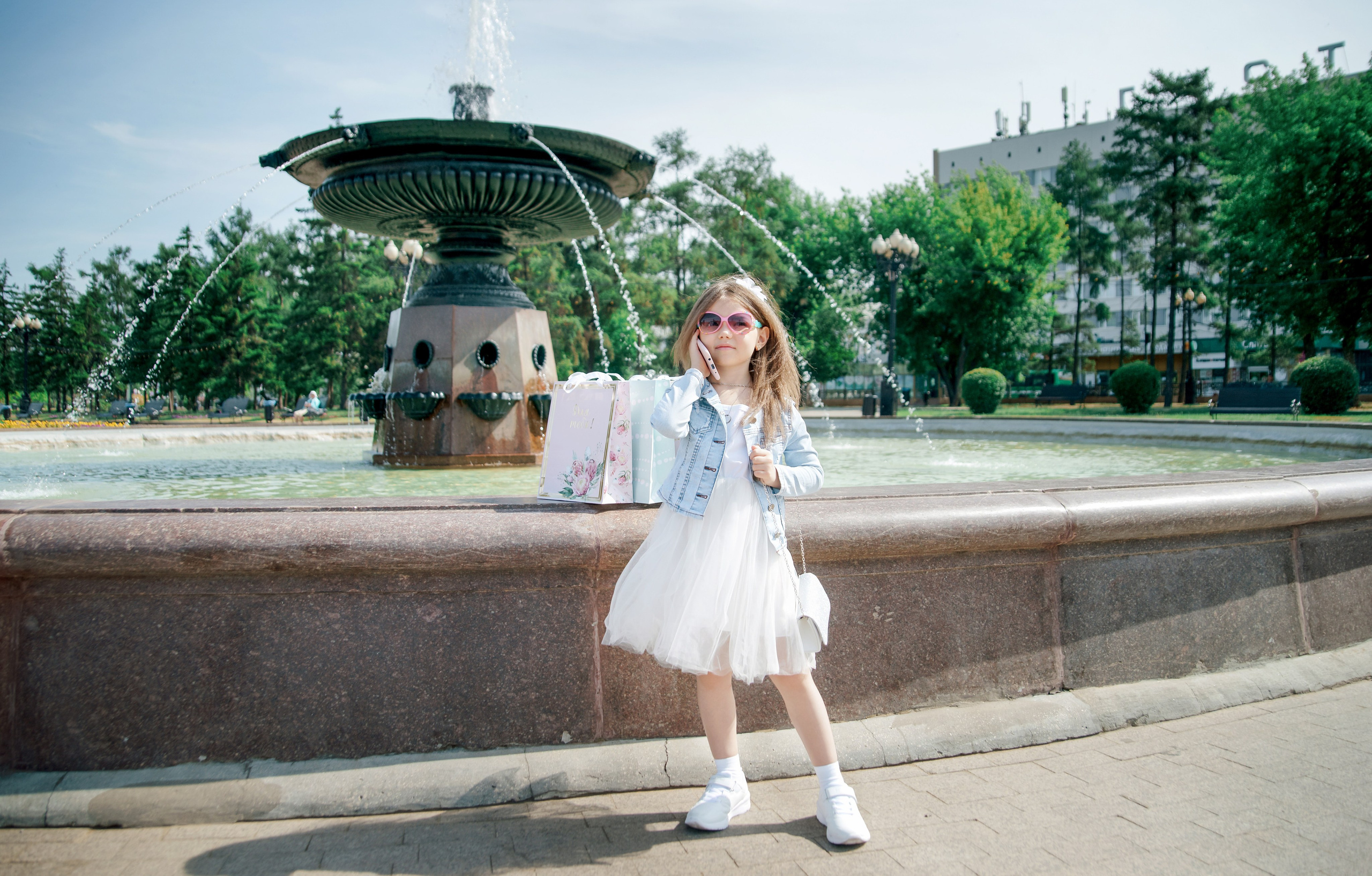 Детская фотосессия летом - девочка стоя у фонтана говорит по телефону