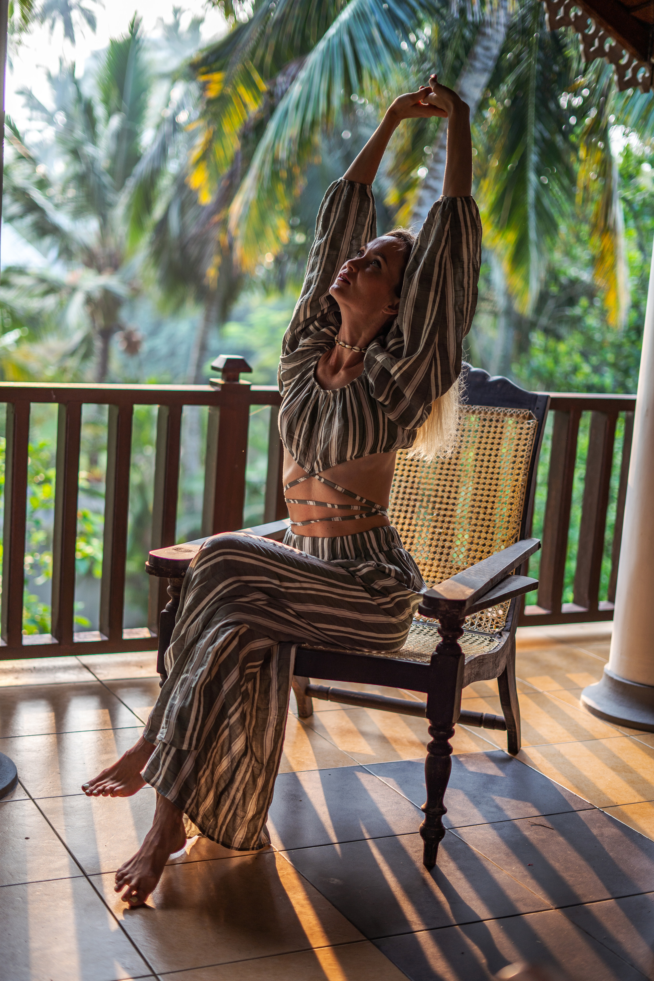 a girl in a striped summer outfit sitting on a chair among palm trees