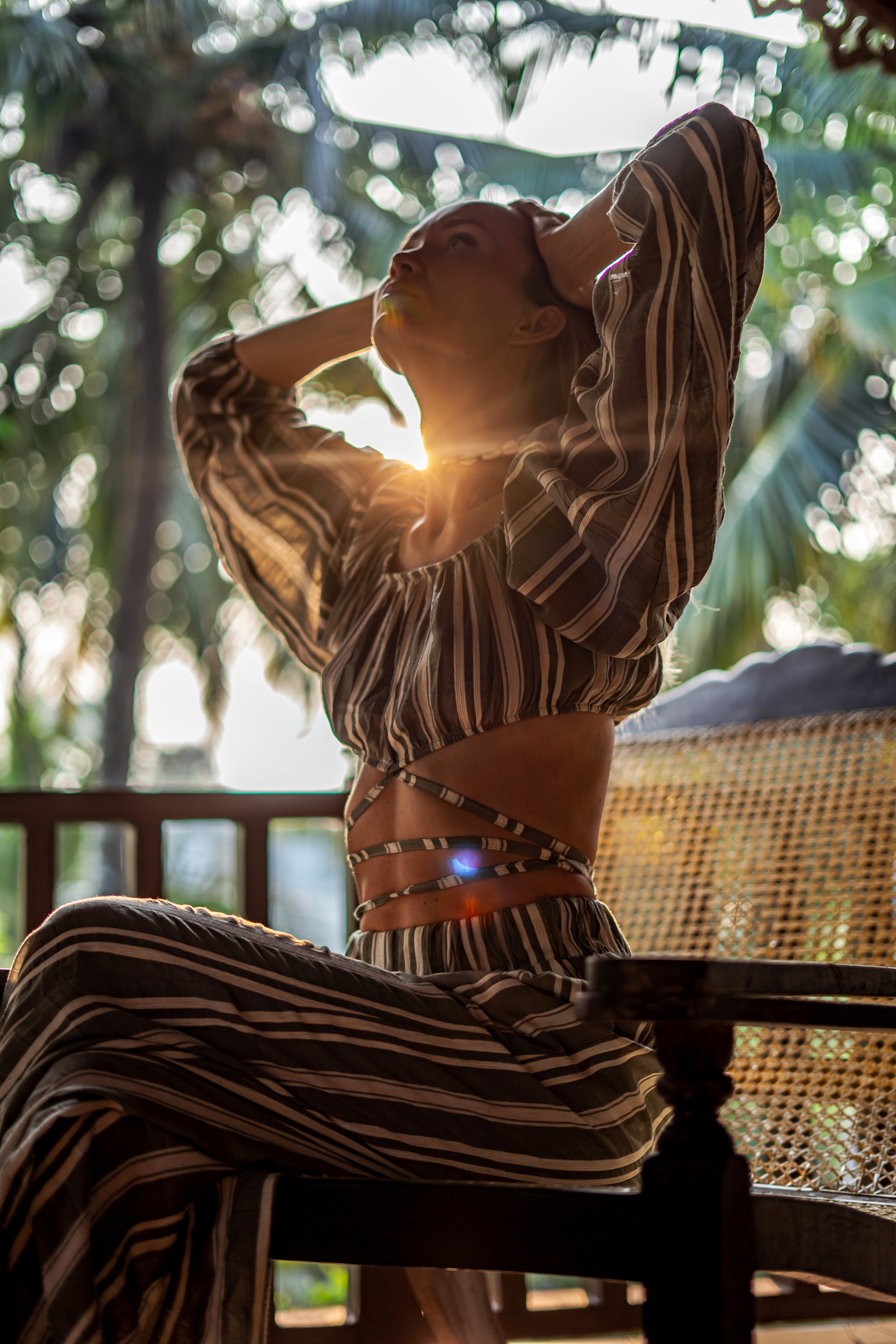 a girl in a summer striped outfit on a chair with palm trees behind her