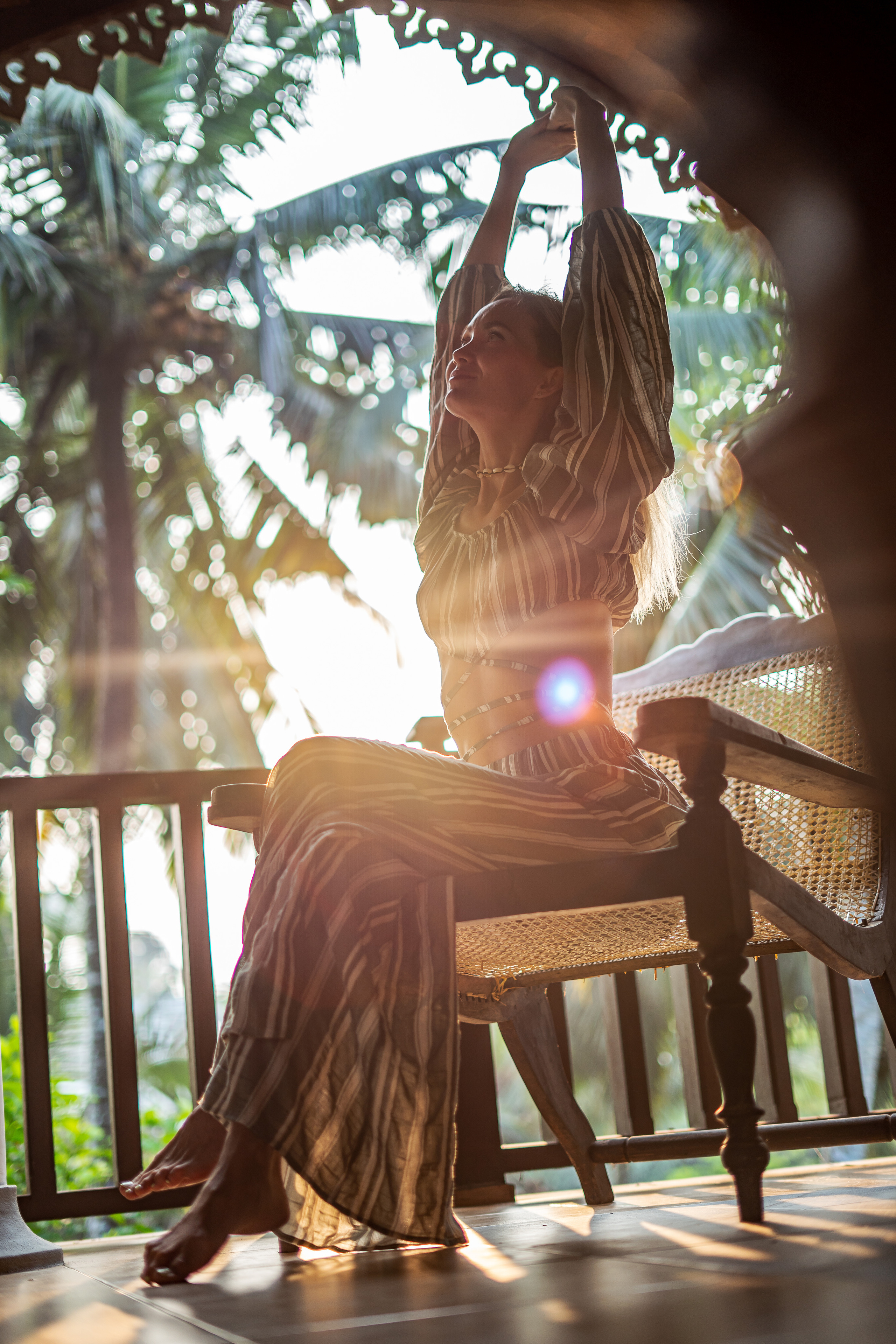 a girl in a striped outfit posing on a chair with palm trees in the background