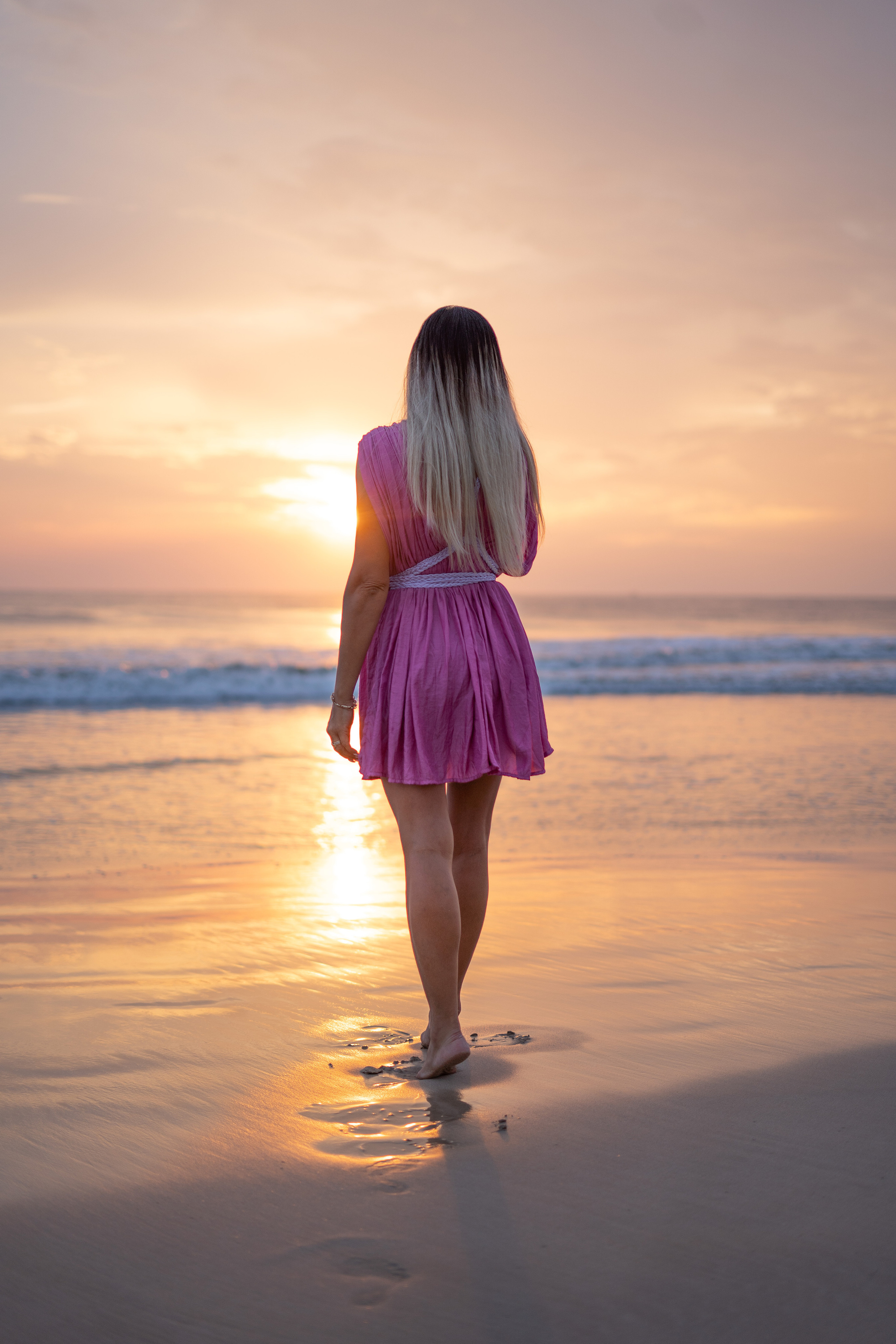a girl walking along the ocean shore at sunset