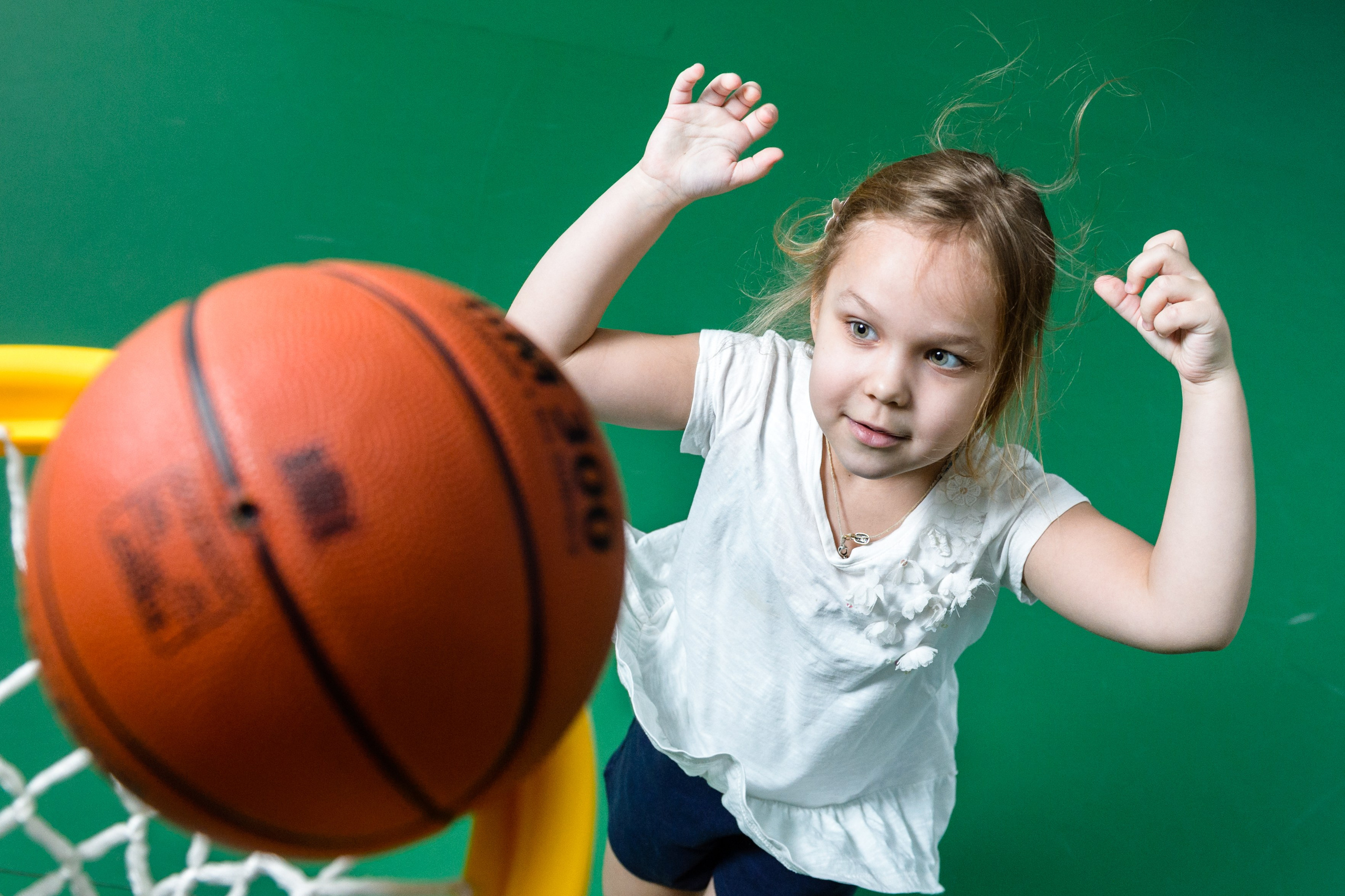 Девочка в спортивном зале кидает баскетбольный мяч в корзину. 