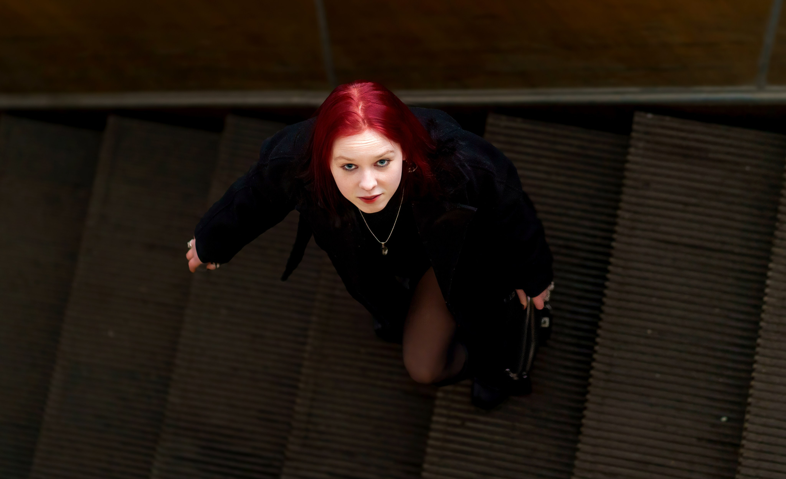 Девушка с красными волосами стоит на ступеньках эскалатора и смотрит в объектив фотографа