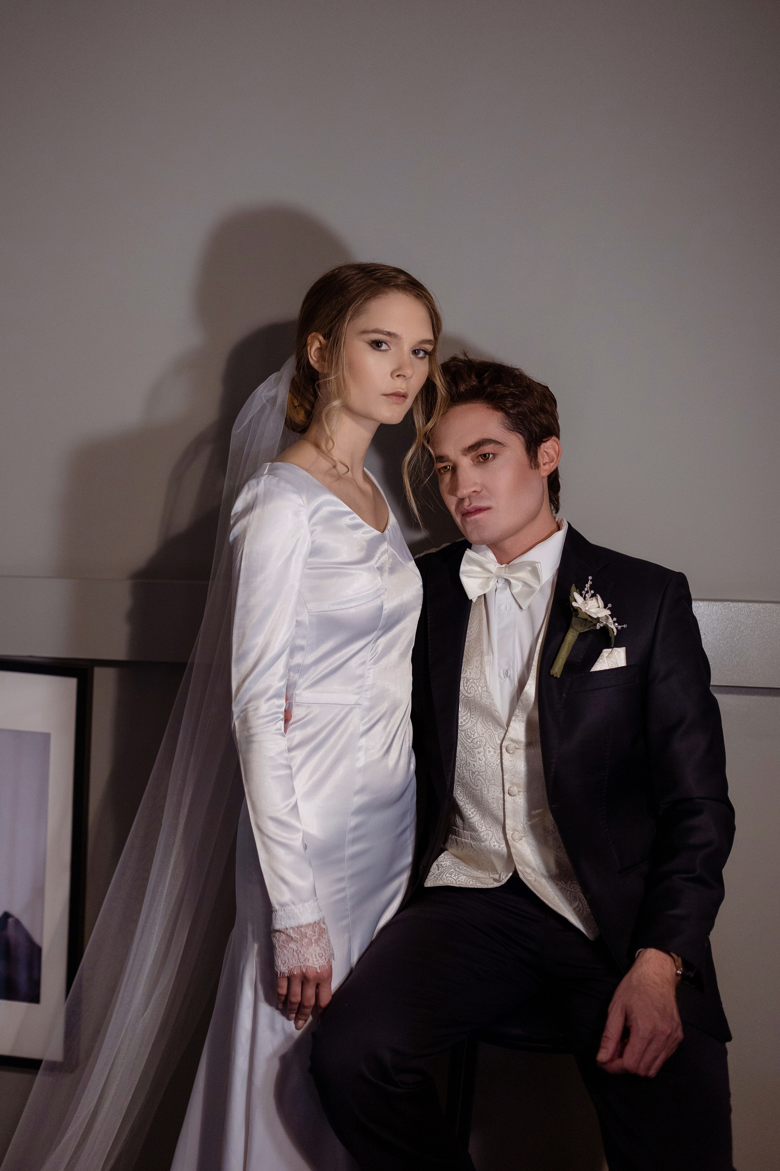 Невеста стоит рядом с сидящим женихом.