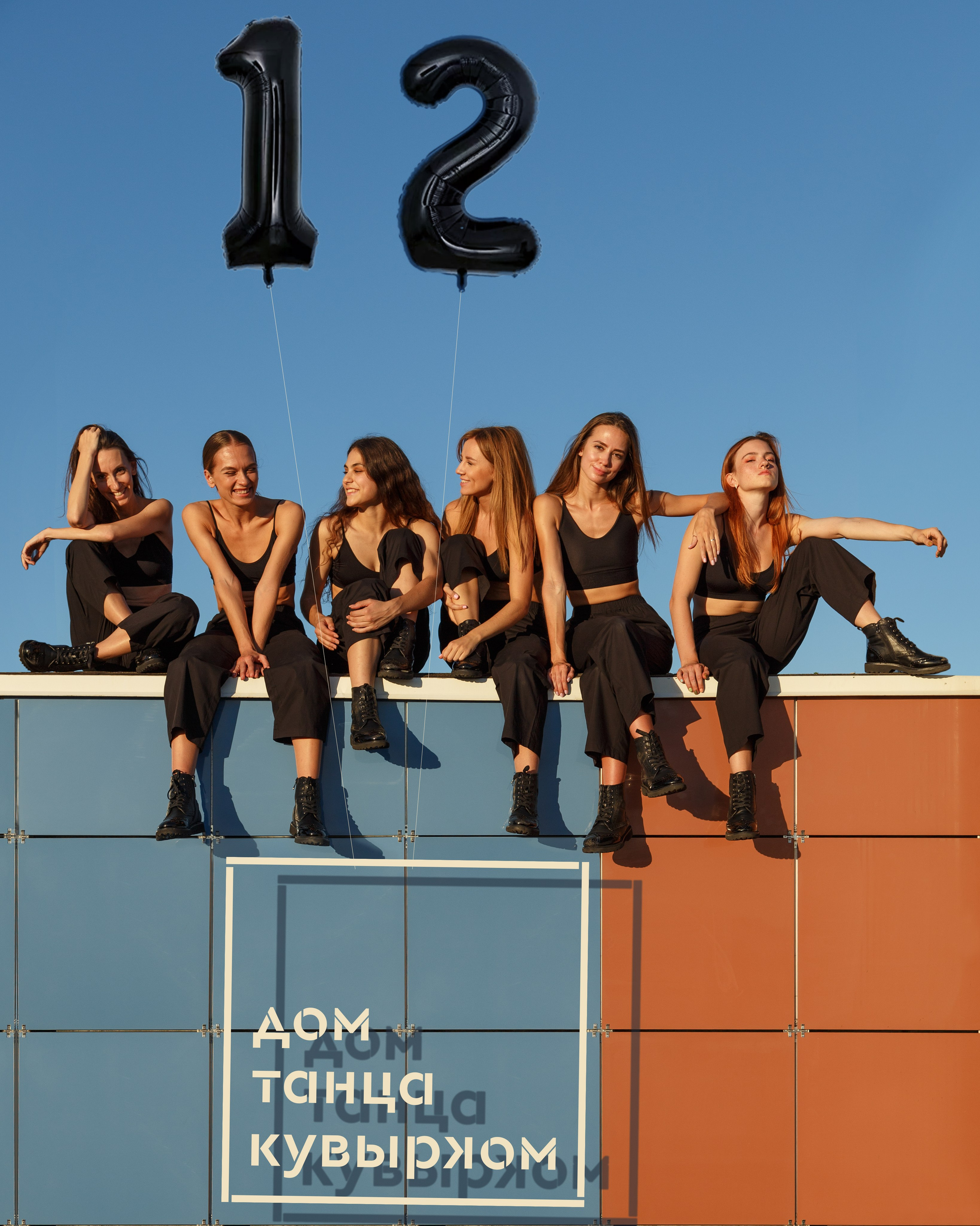 Группа балерин в черных костюмах на фоне неба с шариком '12', фото танцевальной труппы