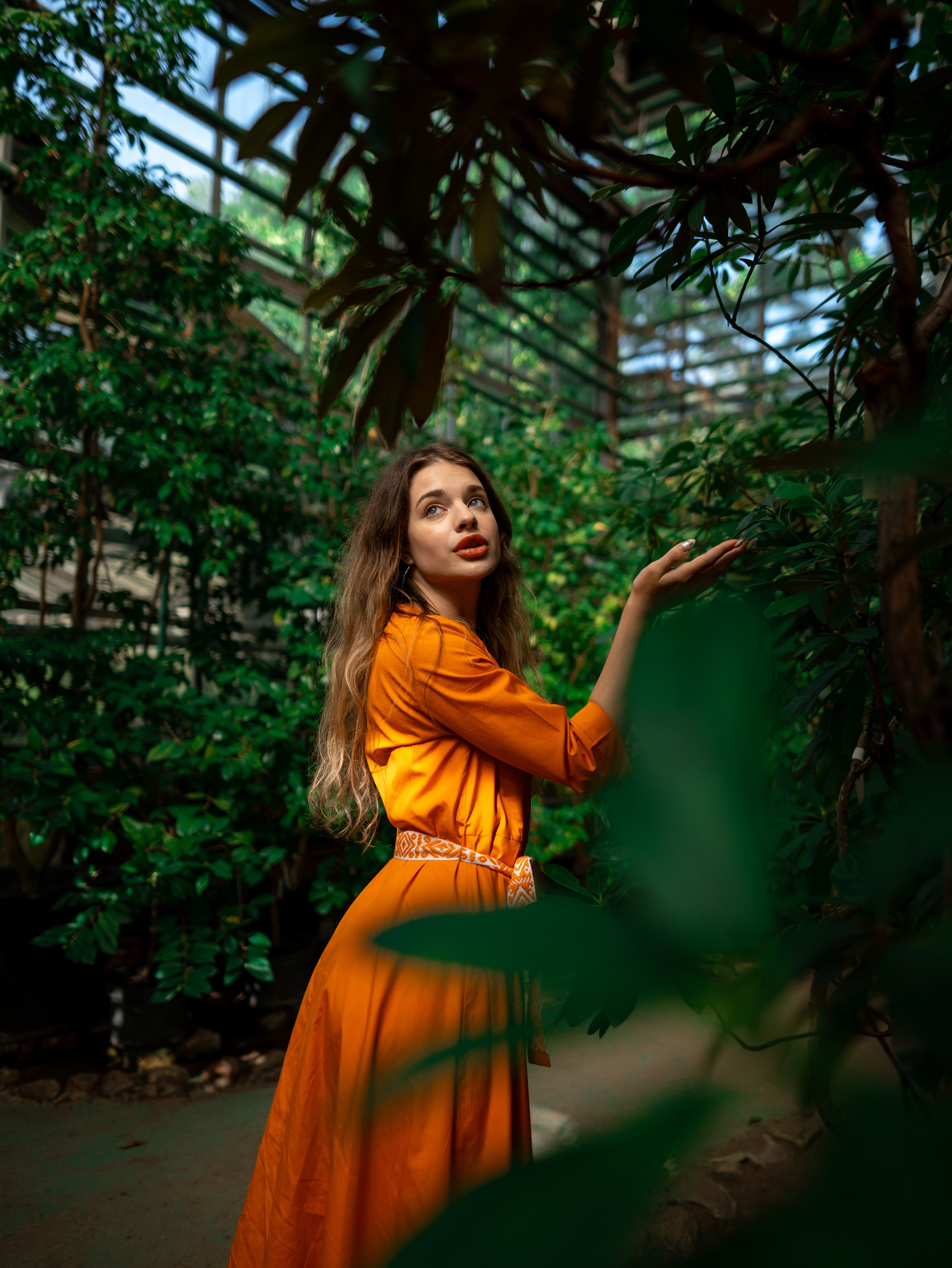 Девушка в оранжевом платье стоит на фоне зелени